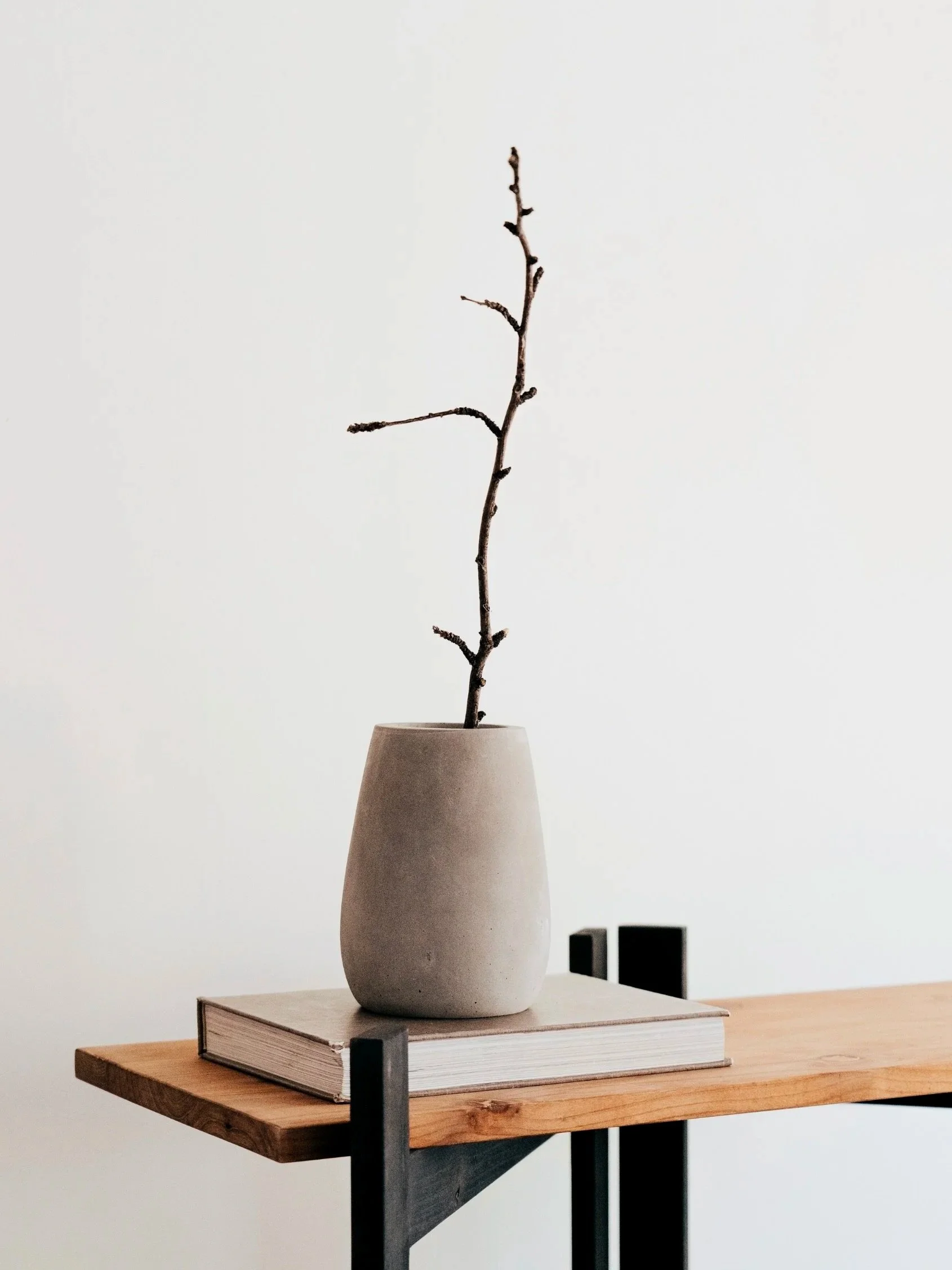 Eine leere Vase mit trockenen Ästen auf einem Buch auf einem Holztisch