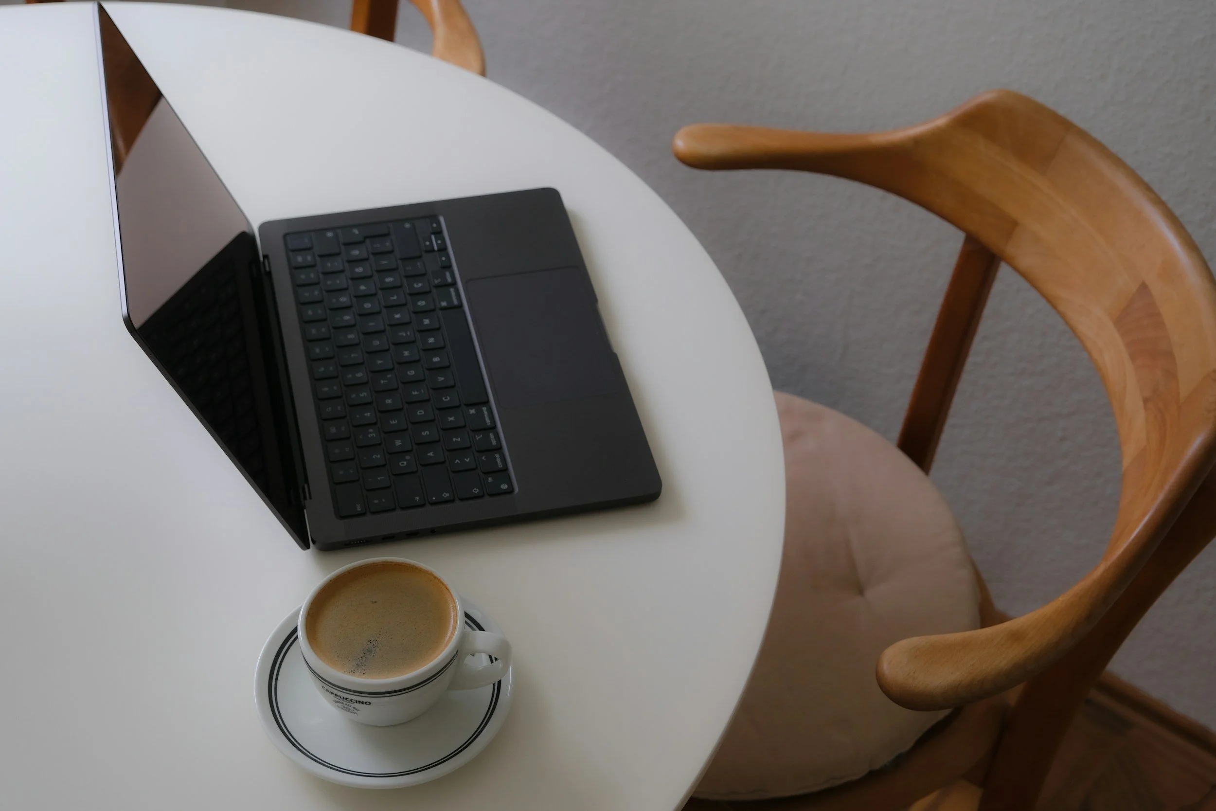 Weißer runder Tisch mit Laptop, Kaffeetasse und Holzstuhl