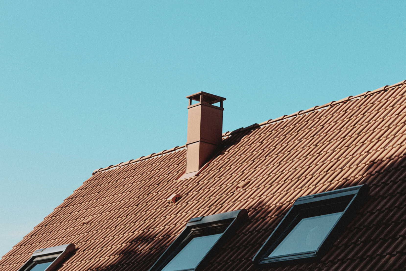 Haus mit brauen Dachziegeln vor blauem Himmel, Foto canva