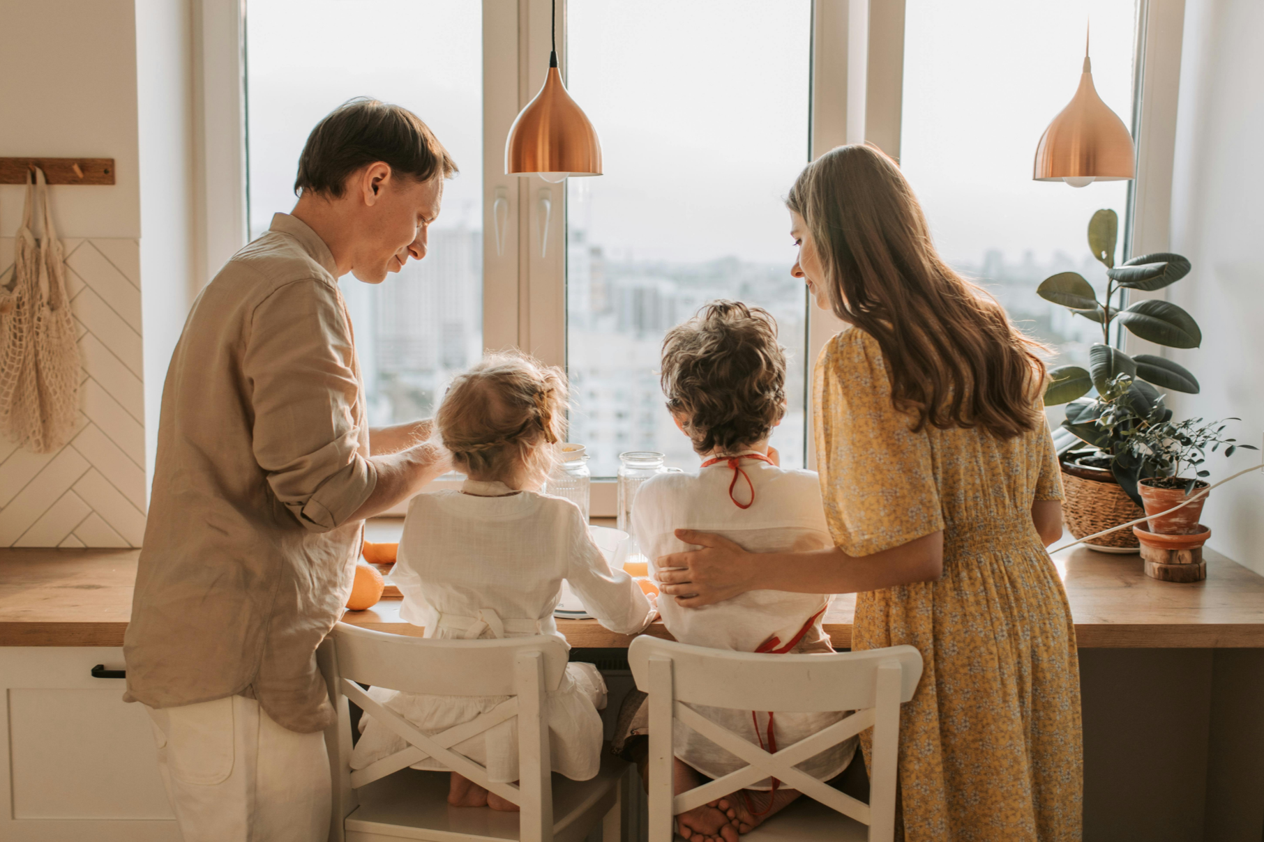 Vater, Mutter und zwei Kinder sitzen am Tisch vor Fenster und Essen, Foto: canva