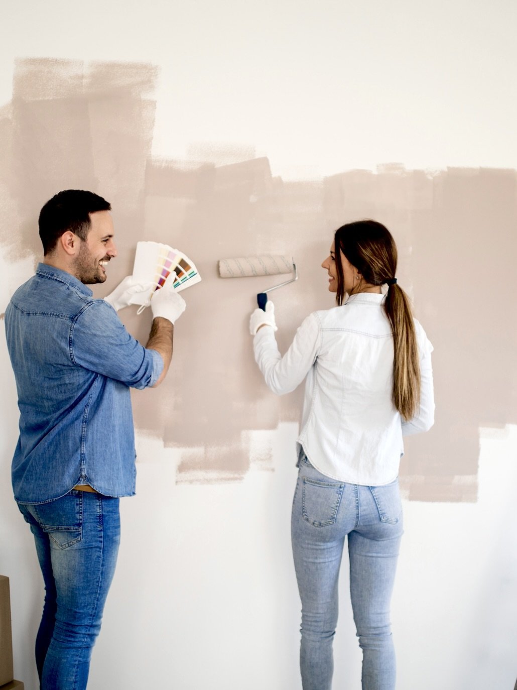 Paar beim Streichen einer Wand, lächelnd, im Hintergrund teilweise gestrichene Wand.