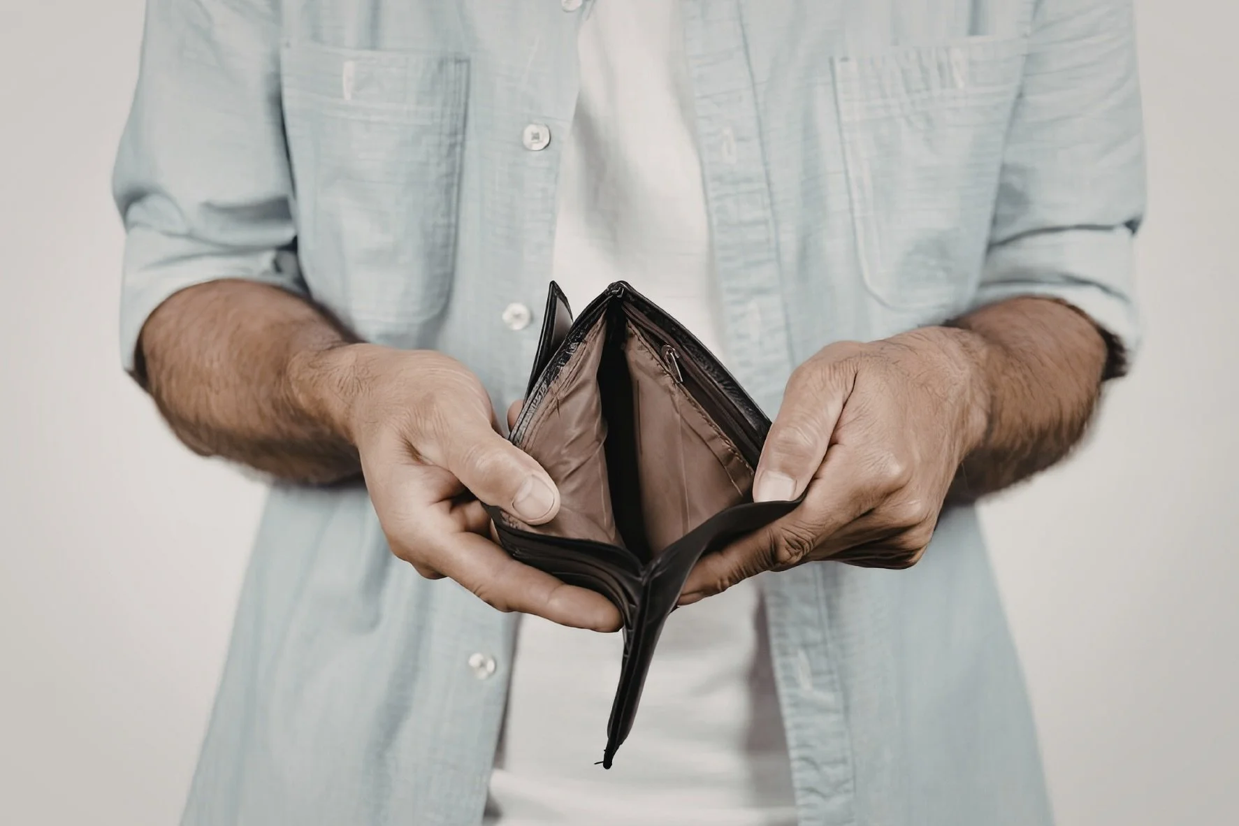 Man in hellem Jeanshemd hält eine leere Geldbörse