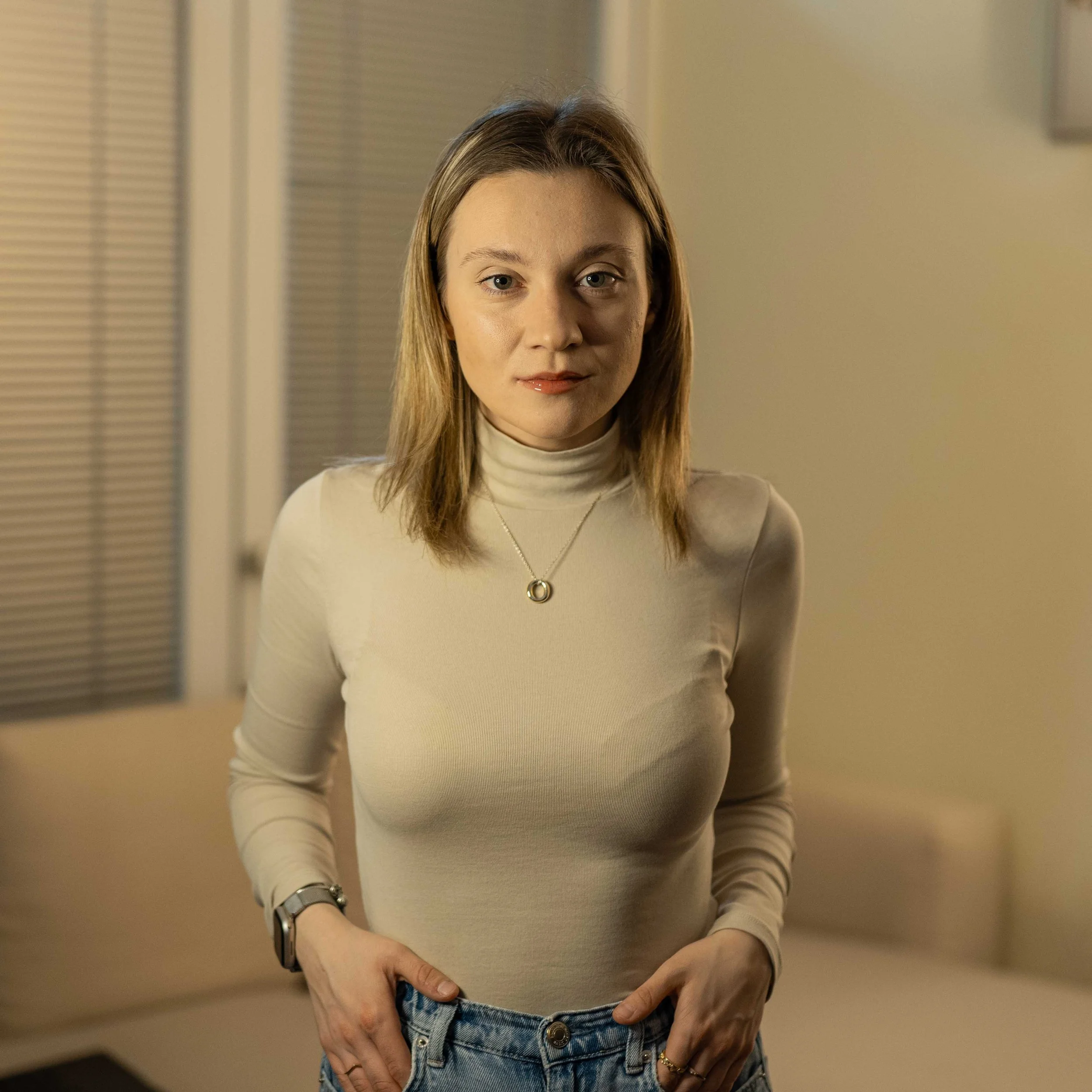 Person wearing a beige turtleneck and jeans indoors.