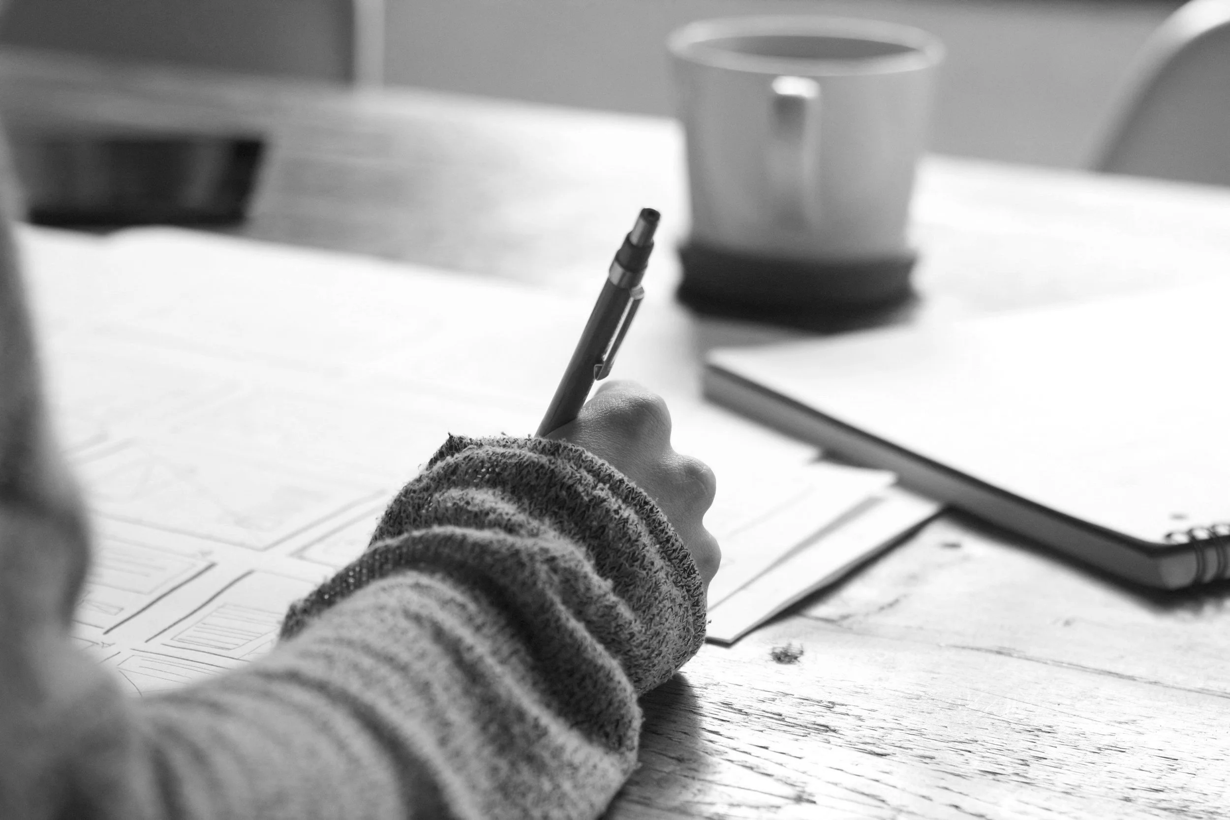 Person writing on paper with pen, coffee mug in background