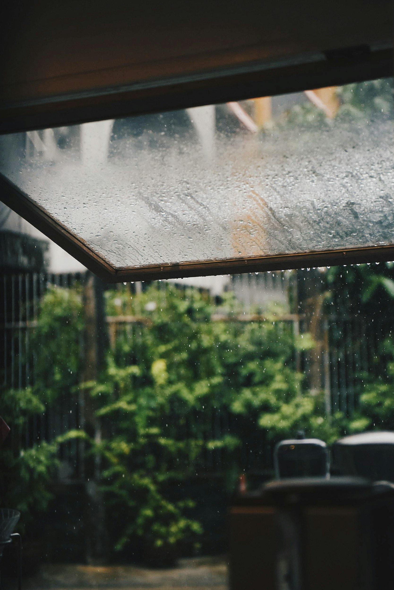 View through a rain-covered window with blurred greenery and an outdoor patio.