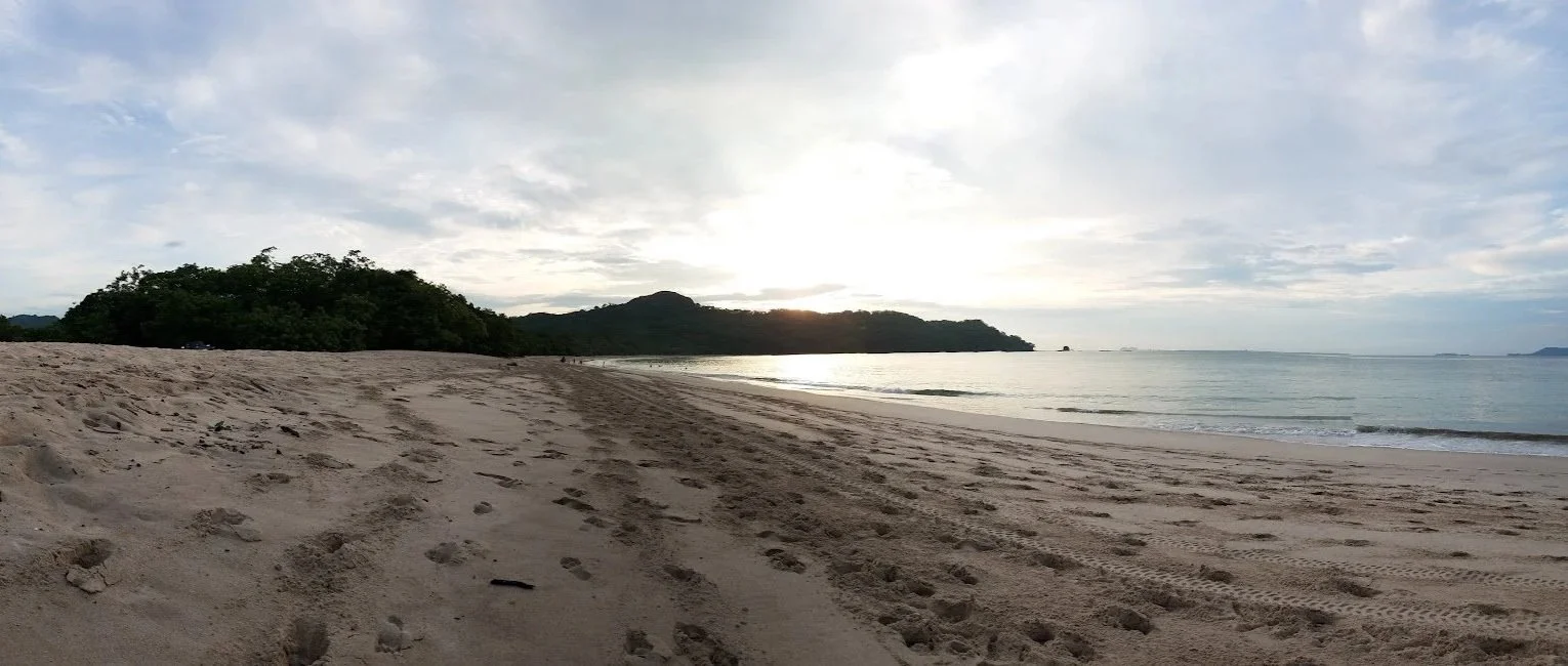 Wide sandy beach at Playa Minas near Tamarindo, Costa Rica, with calm water and green hills in the distance.
