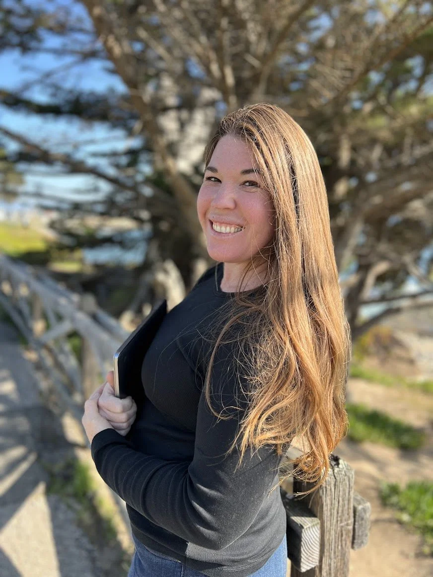Rori Launspach, owner of Lifelong Adventure Travel Boutique, smiling outdoors on West Cliff Drive in Santa Cruz, California.