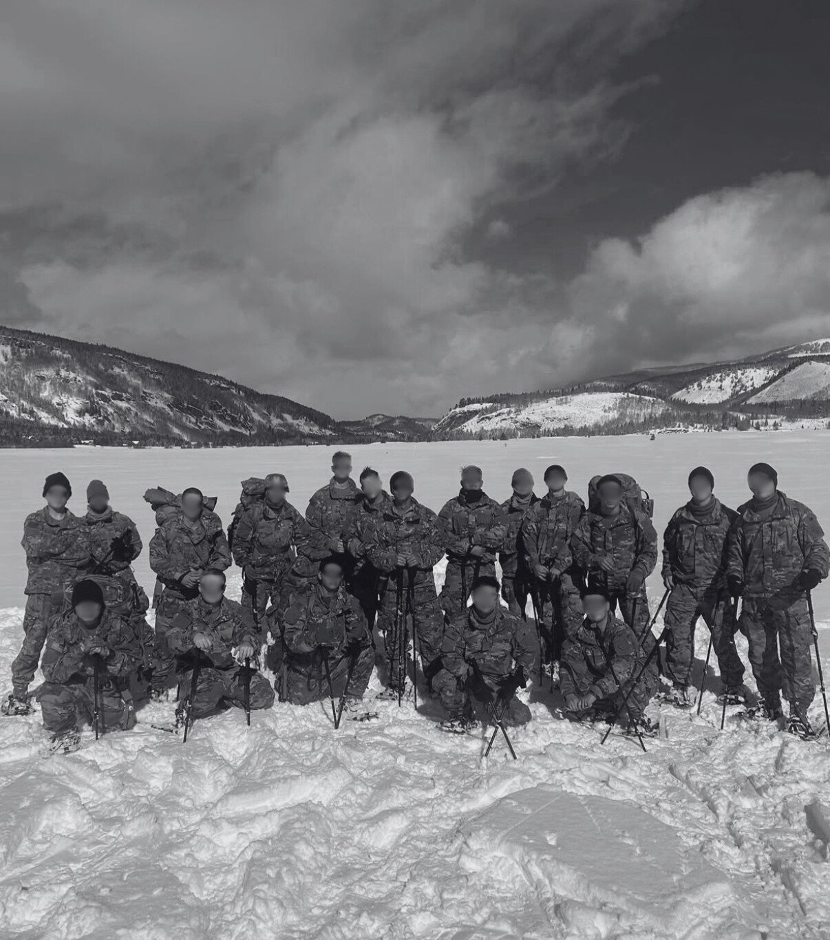Group of soldiers in camouflage uniforms standing in snow with mountains and cloudy sky in the background