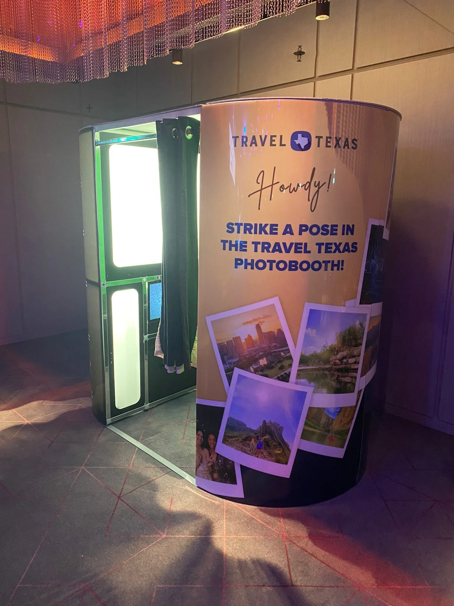 Travel Texas photo booth with a curtain, illuminated frame, and promotional banner featuring photos of Texas landscapes.