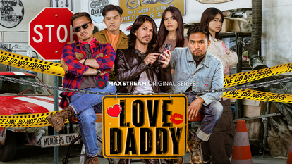 A group of six diverse young adults sitting behind a table with a large sign that says 'LOVE DADDY' and red heart graphics. The scene includes police tape, a stop sign, and caution cones, suggesting a staged or humorous display.