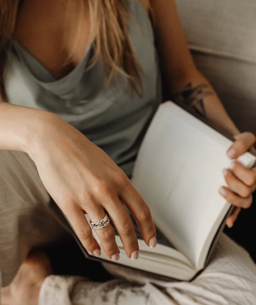 A woman with blonde hair and a tattoo on her arm is holding an open empty notebook or journal with one hand and reaching with the other hand to turn a page.