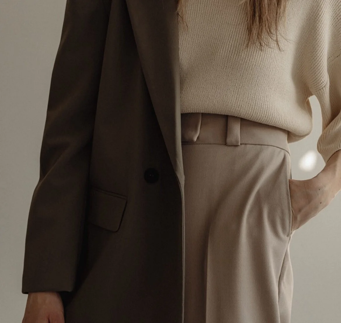 Close-up of a person wearing a beige sweater, beige pants, and a dark brown blazer.