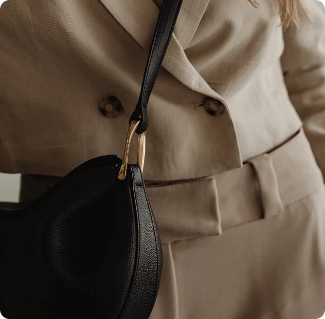 A person wearing a beige blazer and matching pants, carrying a black purse with a gold clasp.