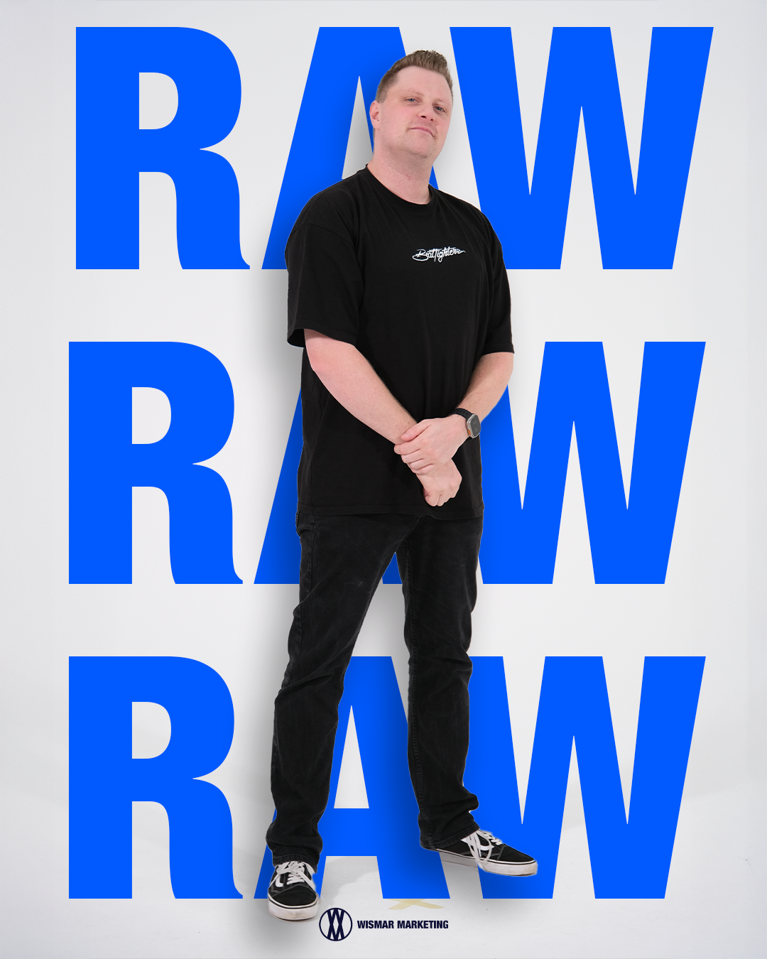 Ein Mann steht vor einem weißen Hintergrund mit großen blauen Buchstaben, die das Wort 'RAW' bilden, und trägt ein schwarzes T-Shirt, schwarze Hosen und Vans-Sneaker @ Wismar marketing