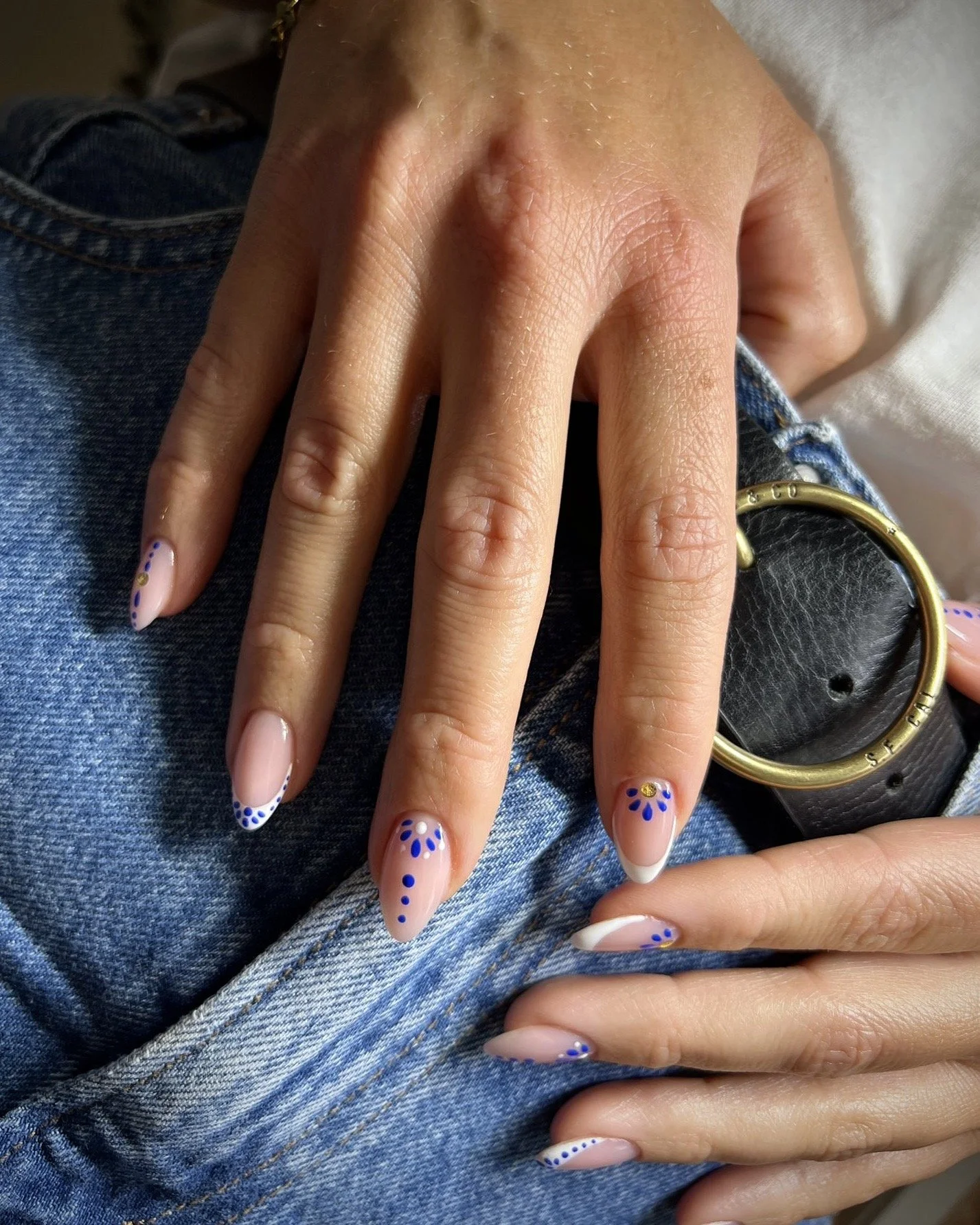 Nahaufnahme von einer Hand mit lackierten Nägeln, die auf eine Jeansjacke liegt, neben einem schwarzen Gürtel mit goldener Schnalle @ Wismar marketing