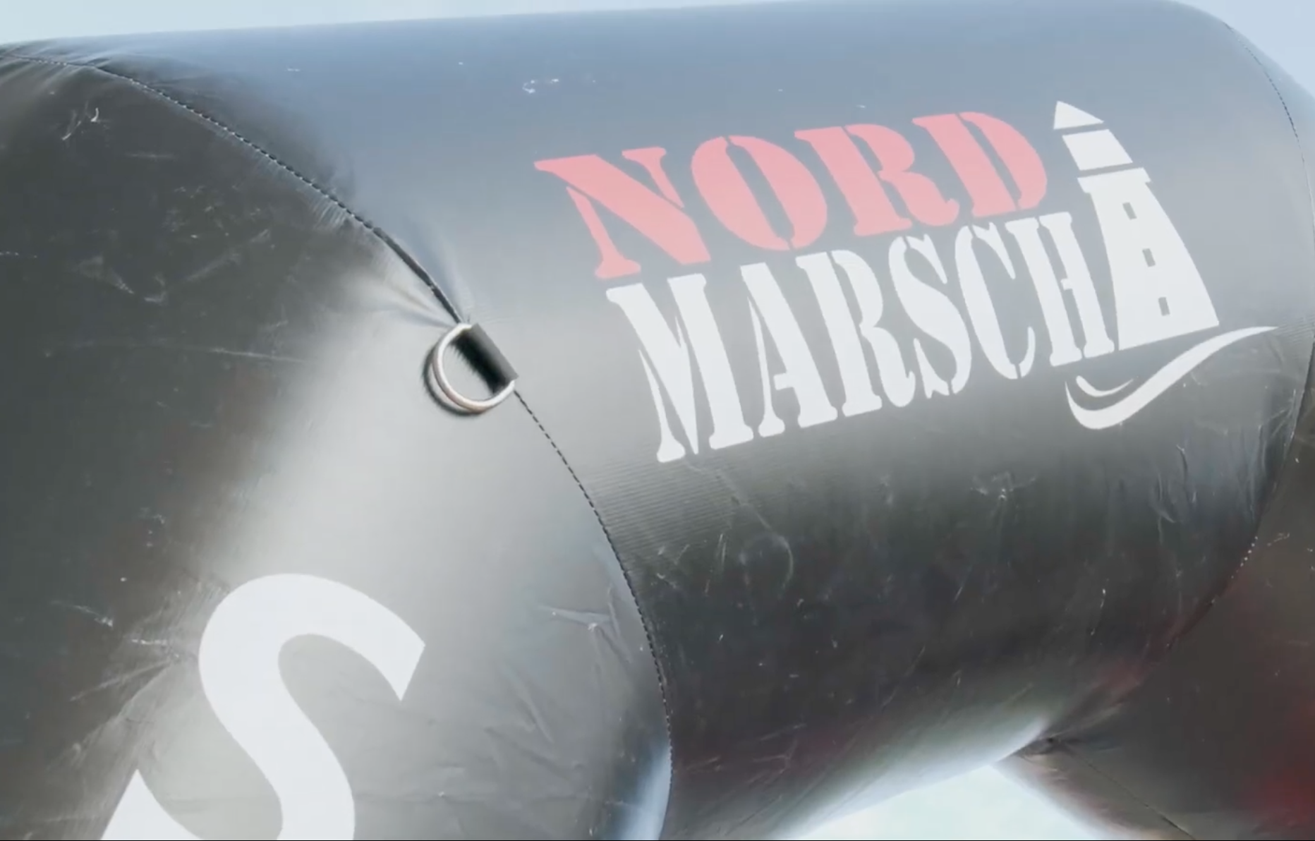 Aufblasbarer Bogen mit Schriftzug "Nord Marsch" und einem Leuchtturmsymbol in Weiß und Rot auf schwarzem Hintergrund. - Wismar-marketing.de