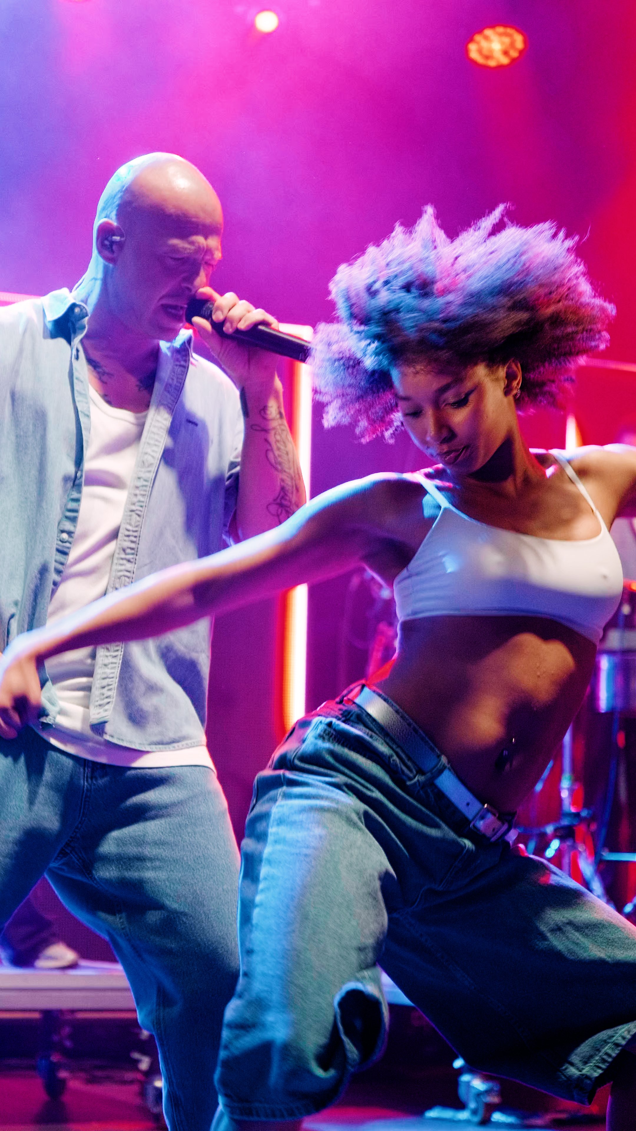 Zwei Menschen tanzen und singen auf einer Bühne bei einem Konzert oder einer Party, mit bunten Lichtern im Hintergrund @ Wismar marketing