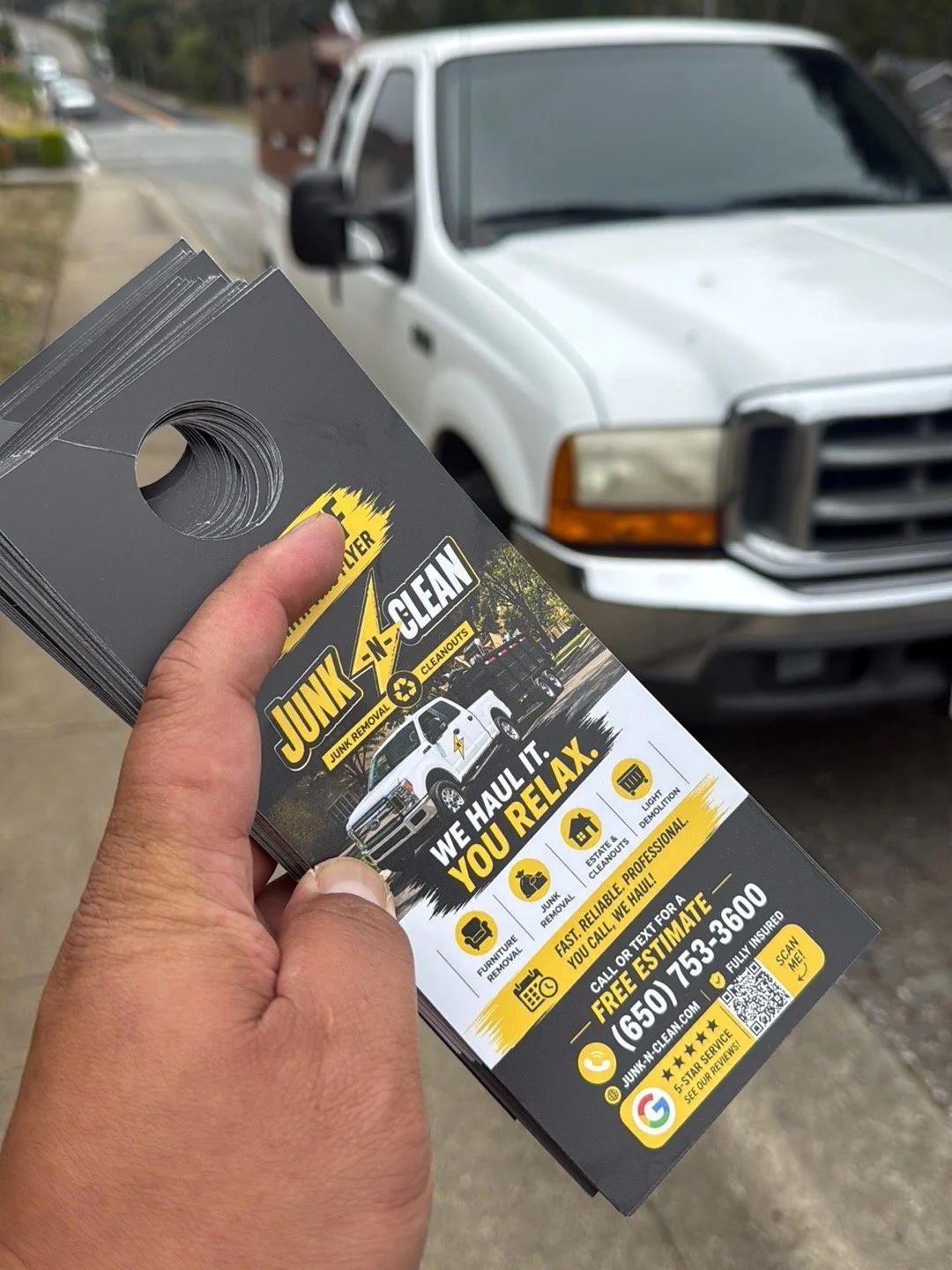A person holding a flyer for Junk N-Clean, a junk removal company, in front of a white truck parked on the street.