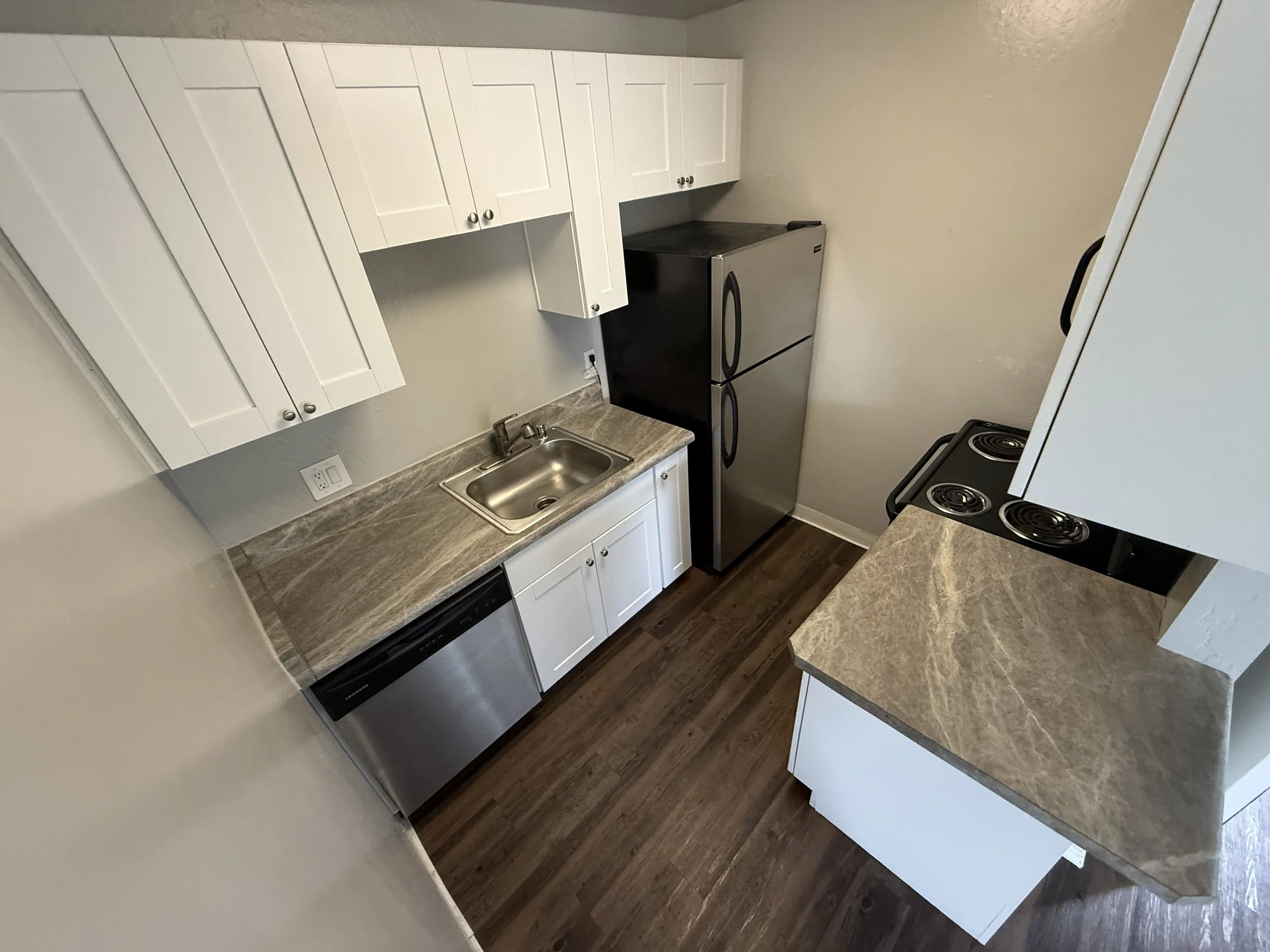 Small kitchen with white cabinets, a stainless steel sink, a black refrigerator, a black stove, and a beige countertop with a wood floor.