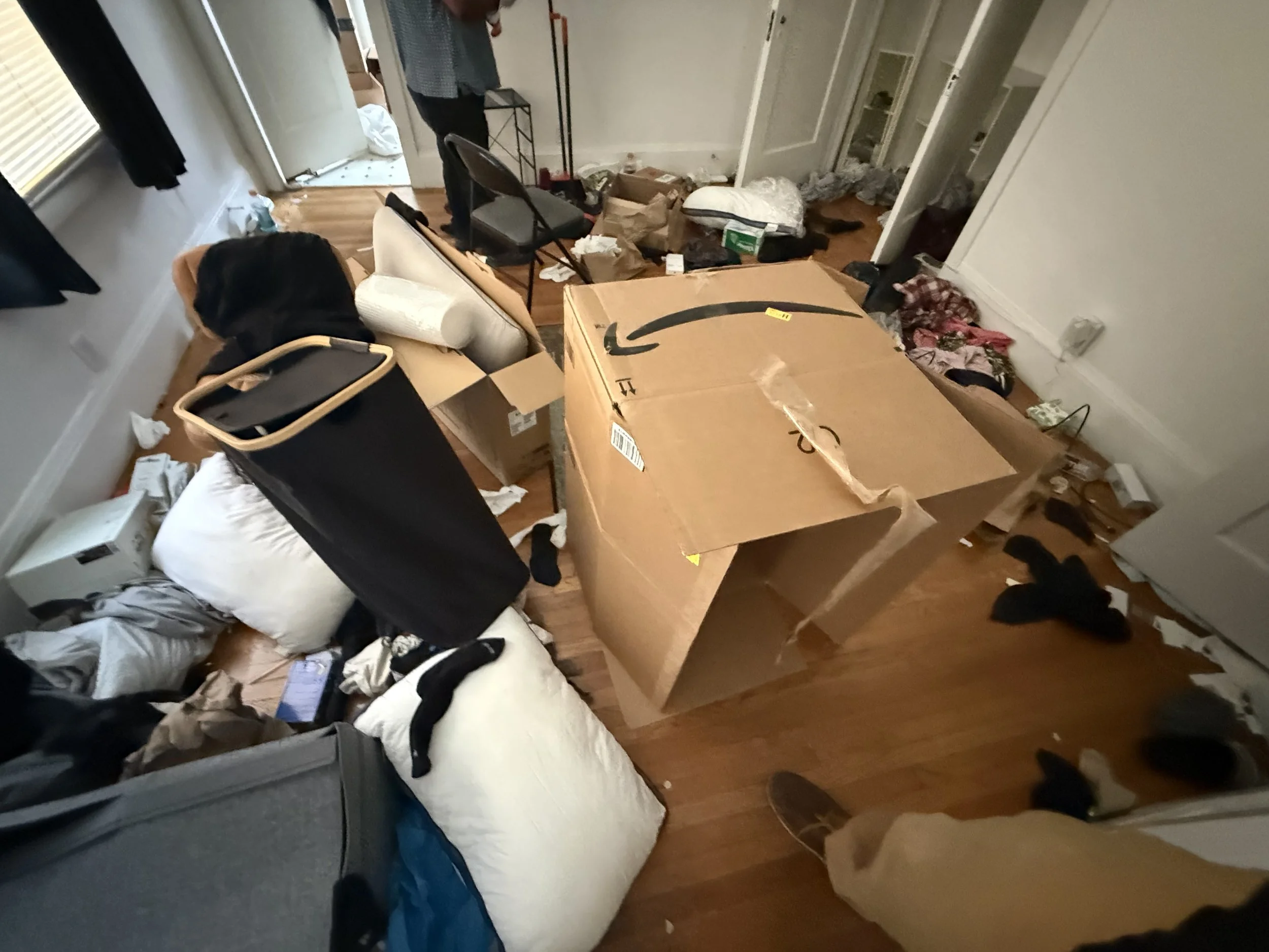 Room with clutter, cardboard box, clothes, mattress, chair, and debris scattered on the floor.