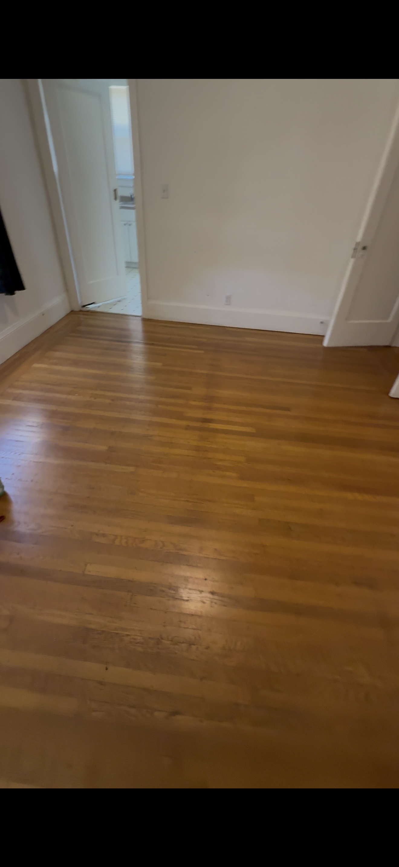 Empty room with hardwood floor and doorway leading to a kitchen area.