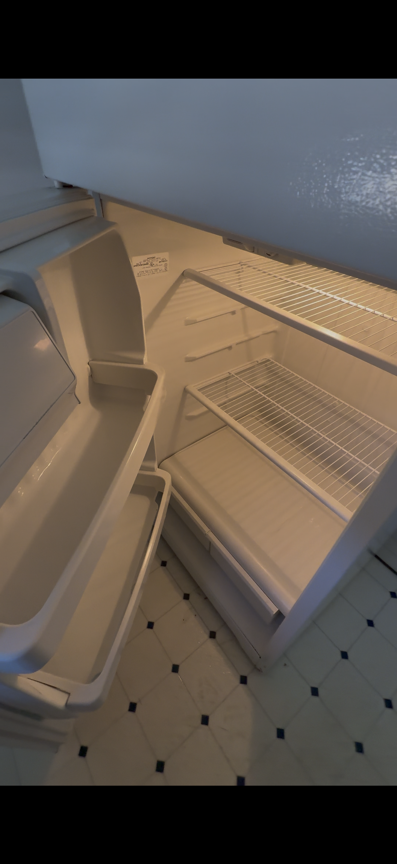 Empty refrigerator with wire shelves, light interior, and tiled floor.