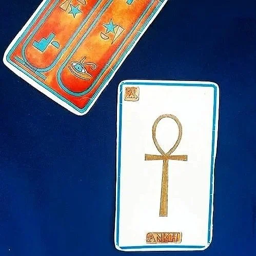 A tarot card with an ankh symbol on a dark blue background, and a partially visible deck of colorful tarot cards in the top left corner.