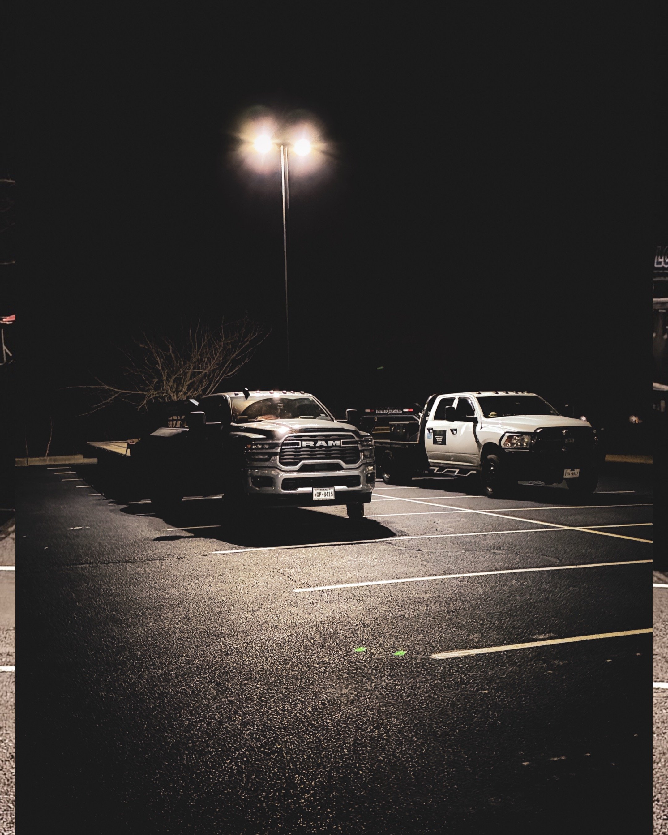 A night scene in a parking lot illuminated by a single streetlamp, with three pickup trucks parked and empty spaces around them.