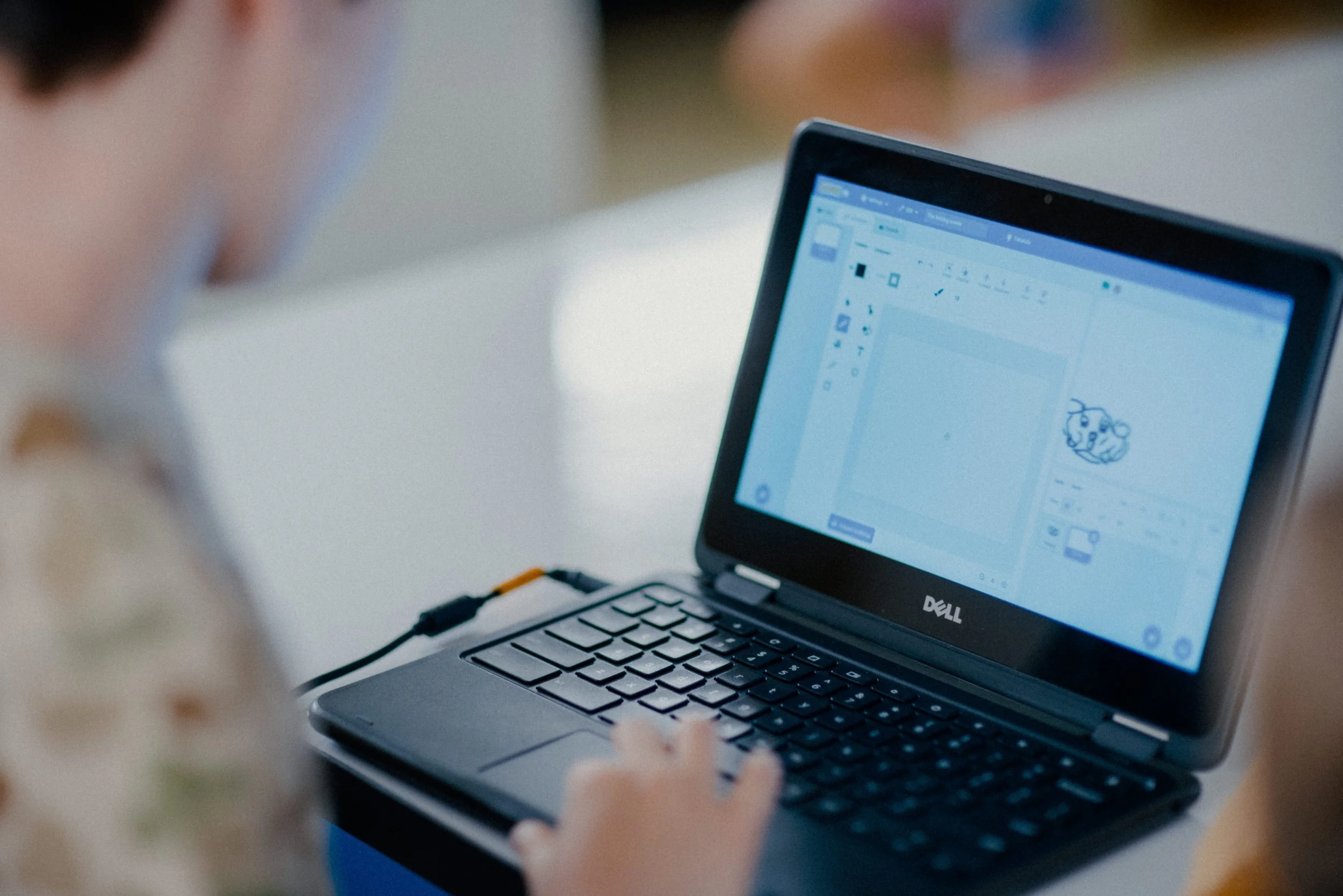 Child using a Dell laptop with drawing software open on the screen, depicting a cartoonish character.