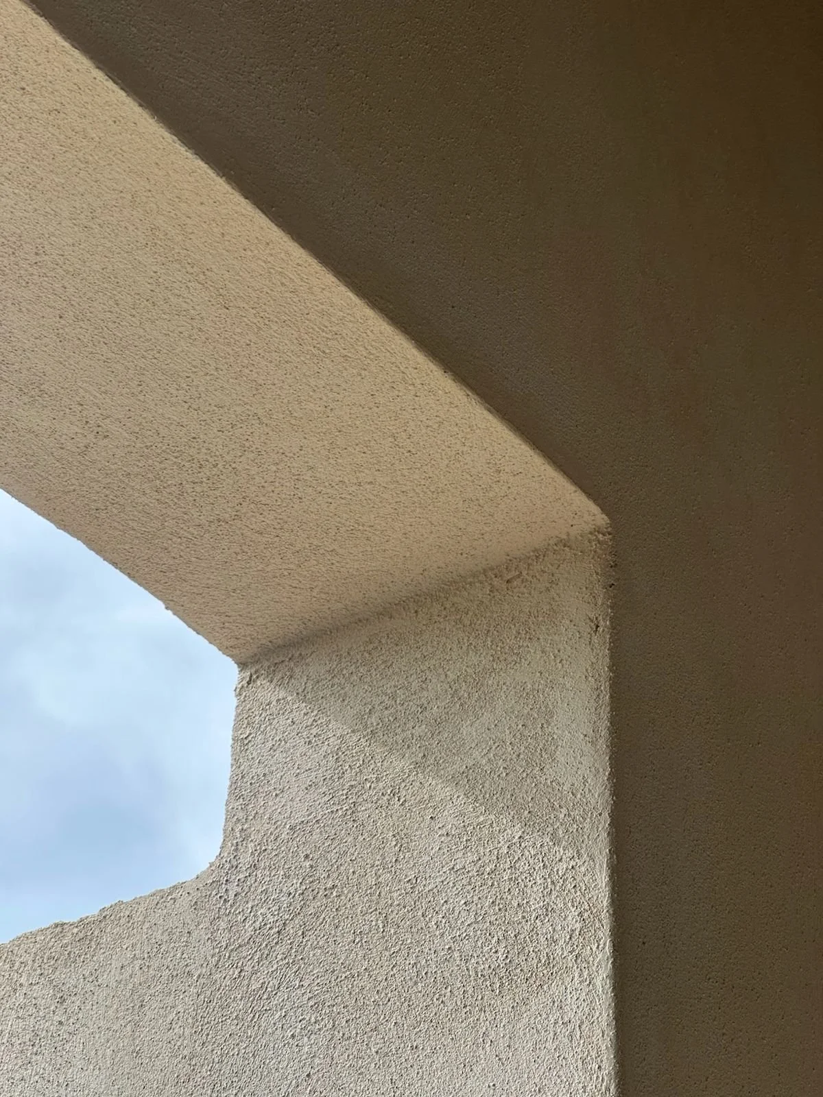 Close-up of a textured beige stucco corner of a building with the sky visible in the background.