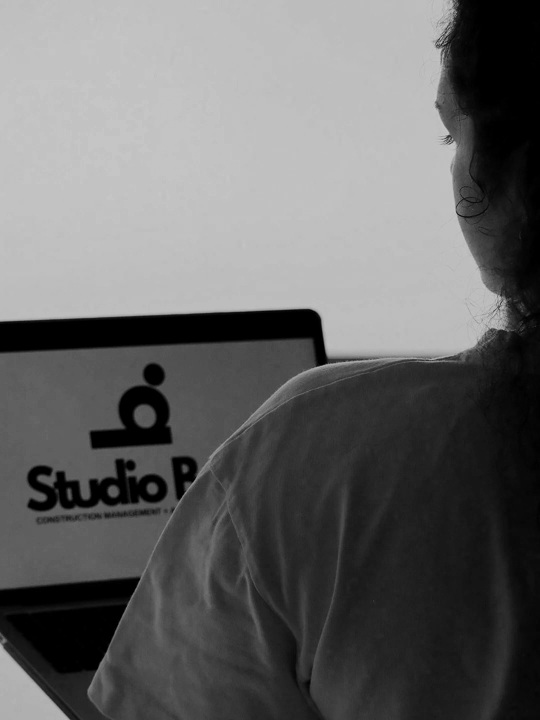 A woman with curly hair viewed from behind working on a laptop with a logo that says "Studio B" on the screen.