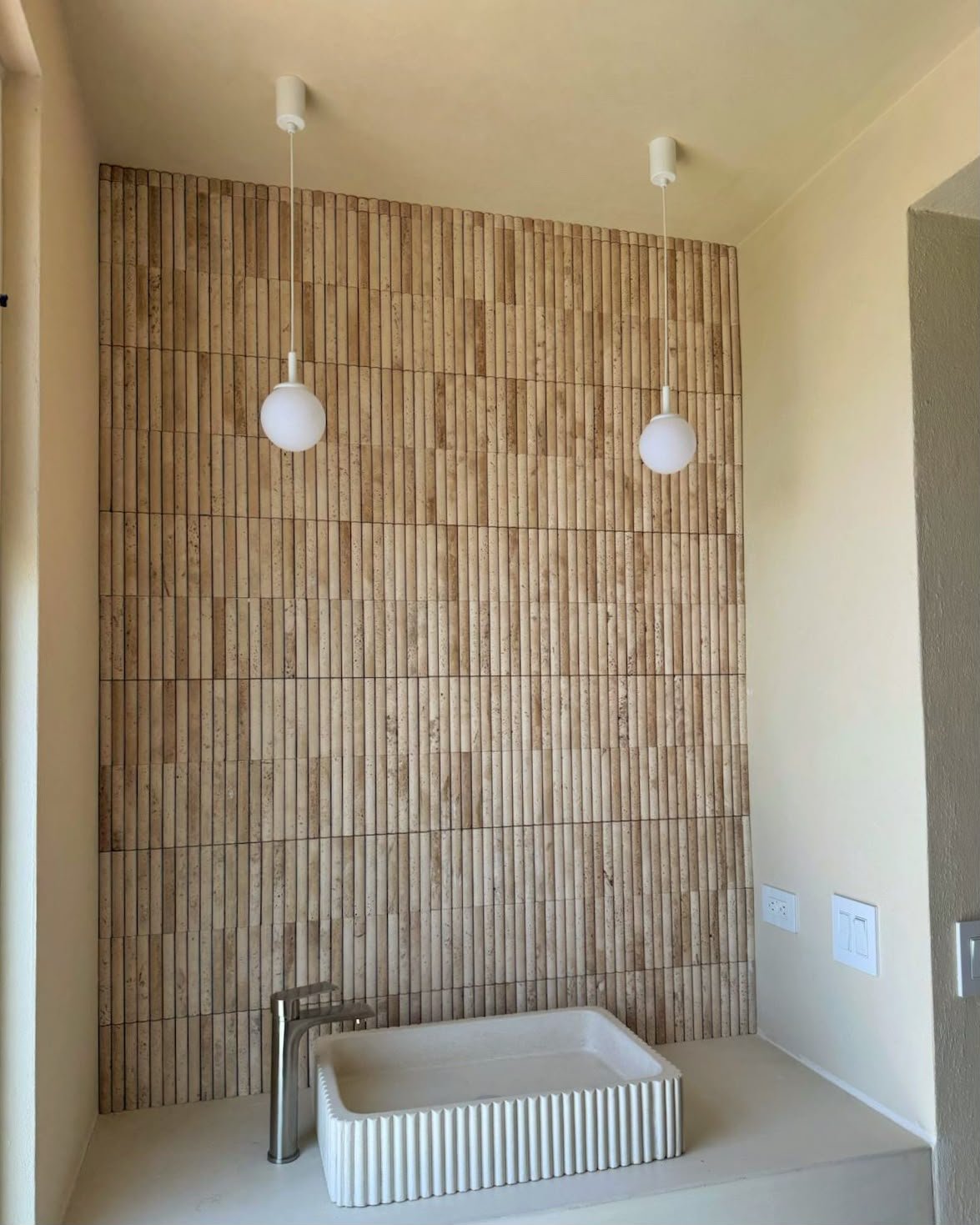 Interior of a room with a textured wooden accent wall, two hanging pendant lights, a small white basin, and electrical outlets.