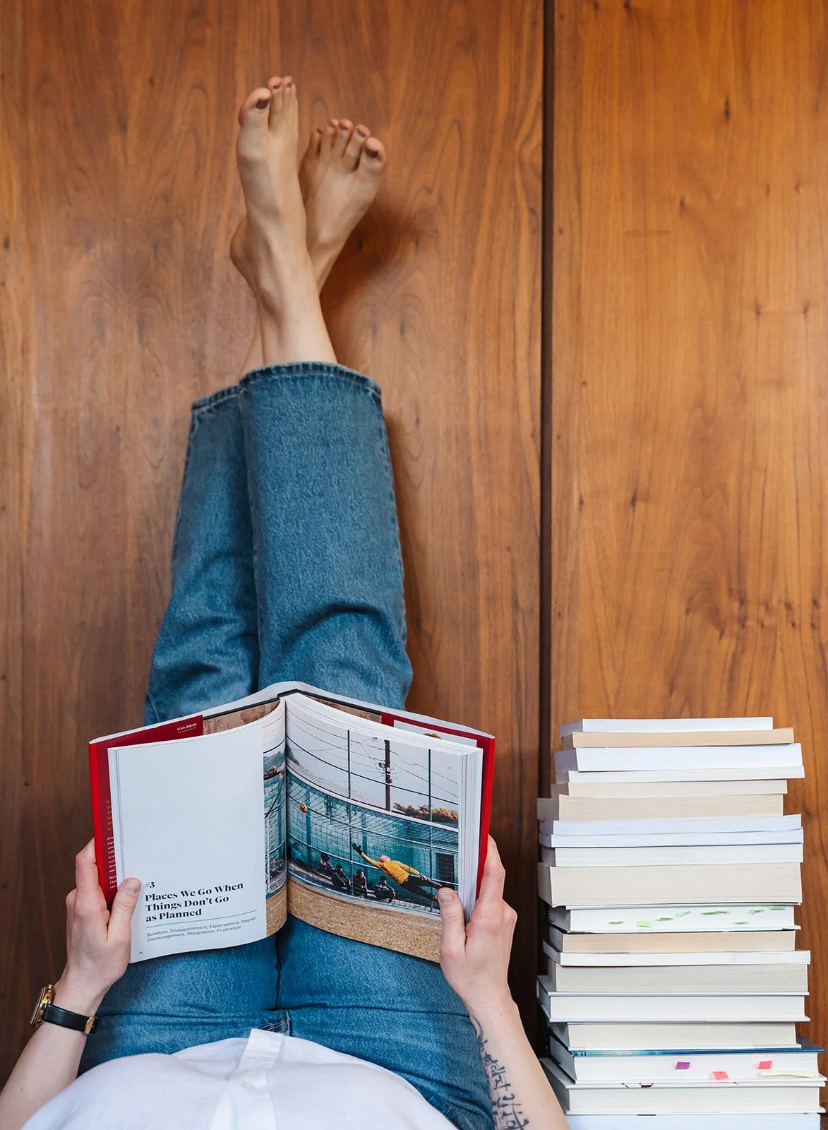 Woman reading a book with legs in the air next to a stack of books