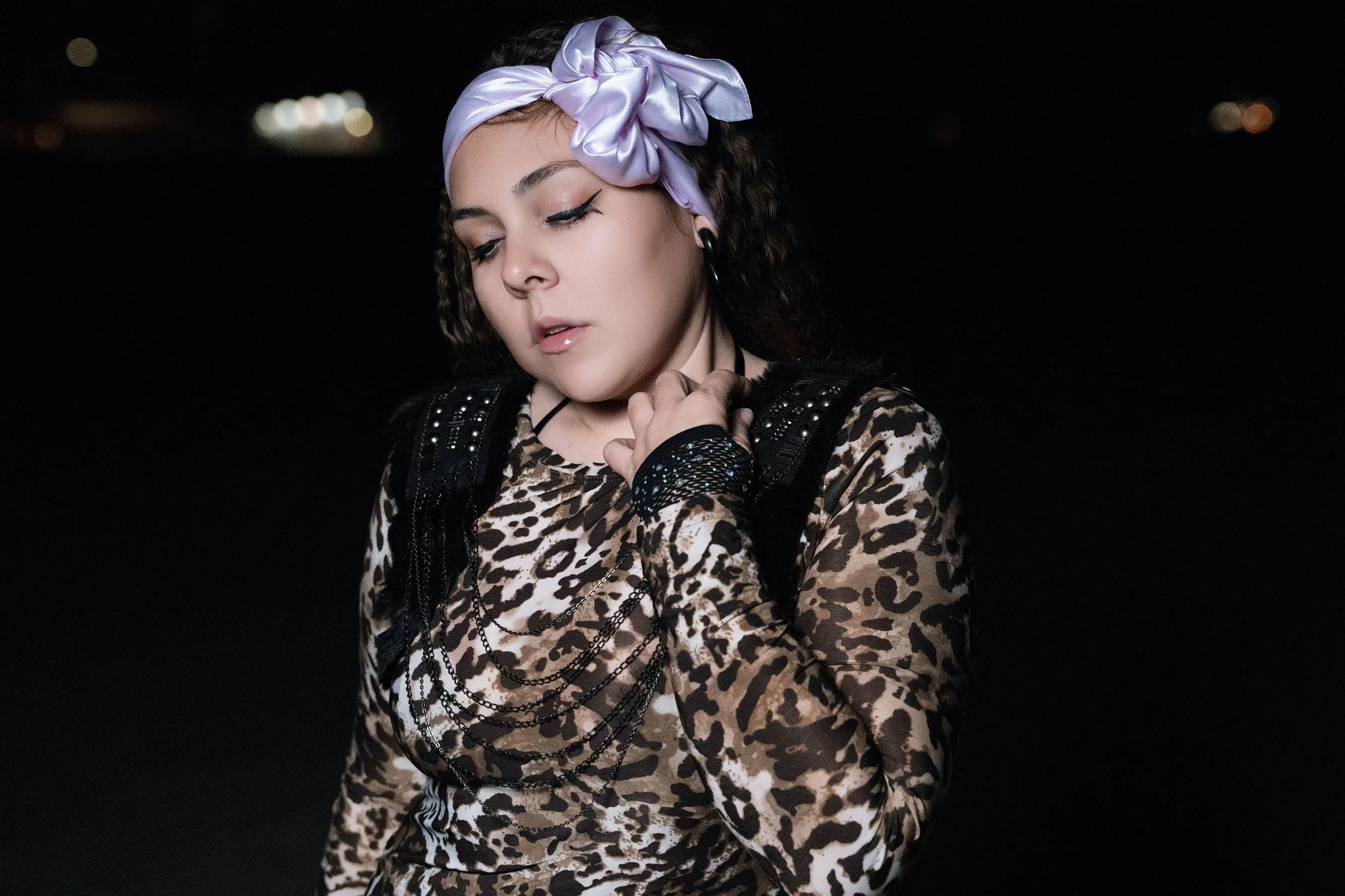 Person wearing a leopard print top and a pink ribbon headband against a dark background.