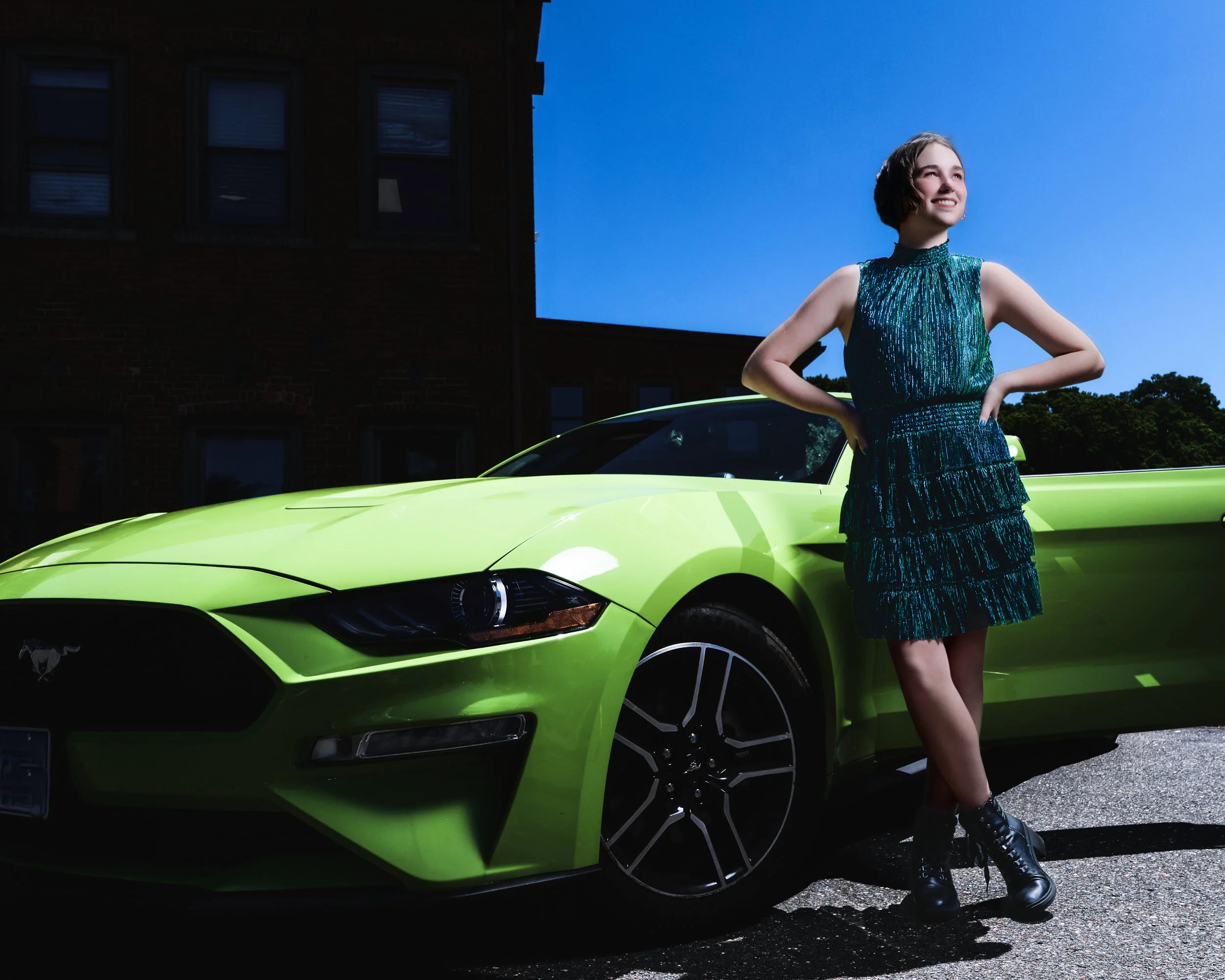 Woman in a green dress posing beside a bright green sports car in front of a brick building.