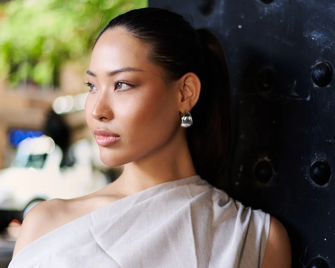 Woman wearing a one-shoulder top posing for a natural-light fashion portrait in New York City.