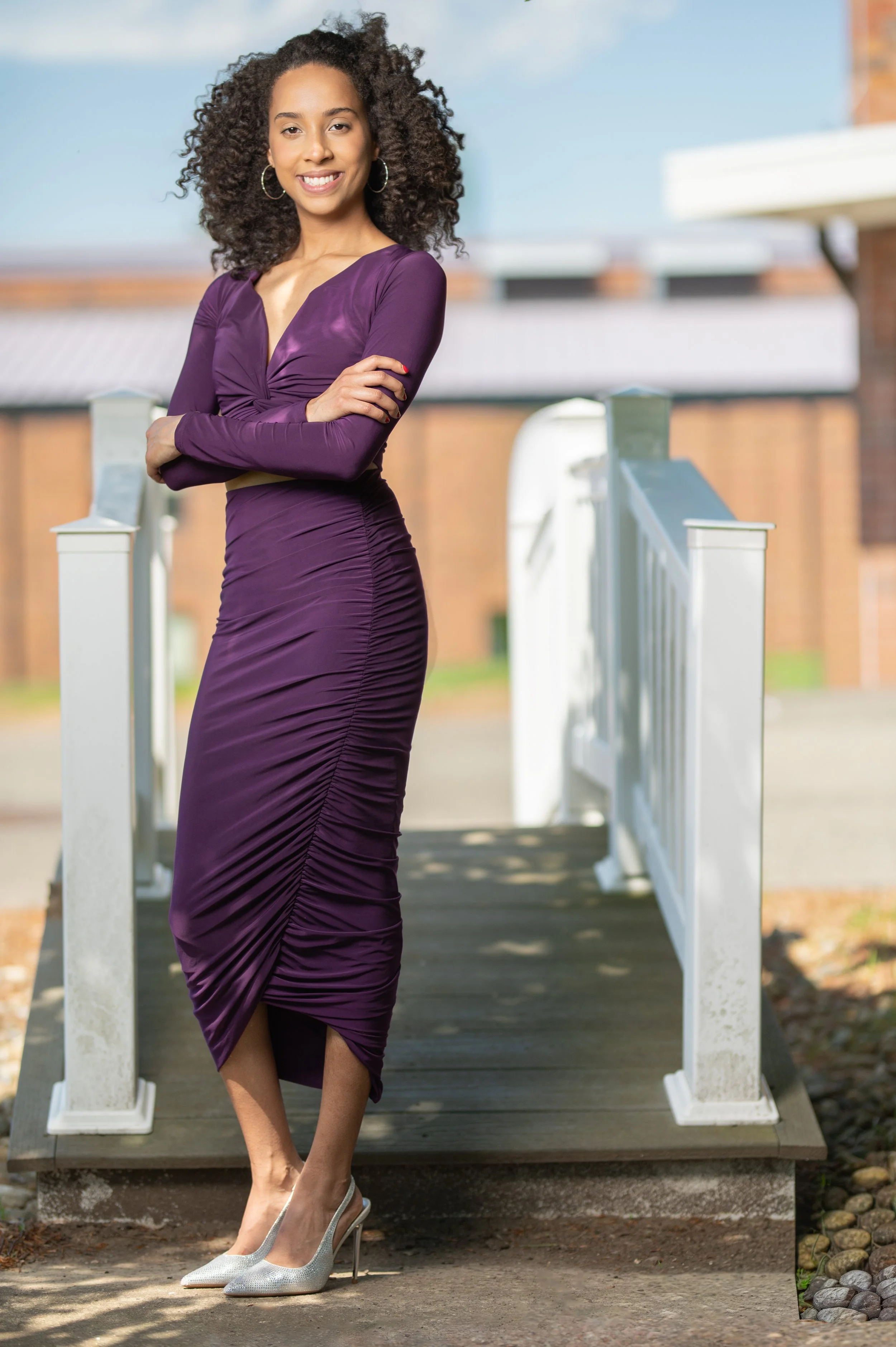 Fashion-inspired senior portrait of a graduate with natural curly hair, photographed outdoors with soft light and a blurred background.