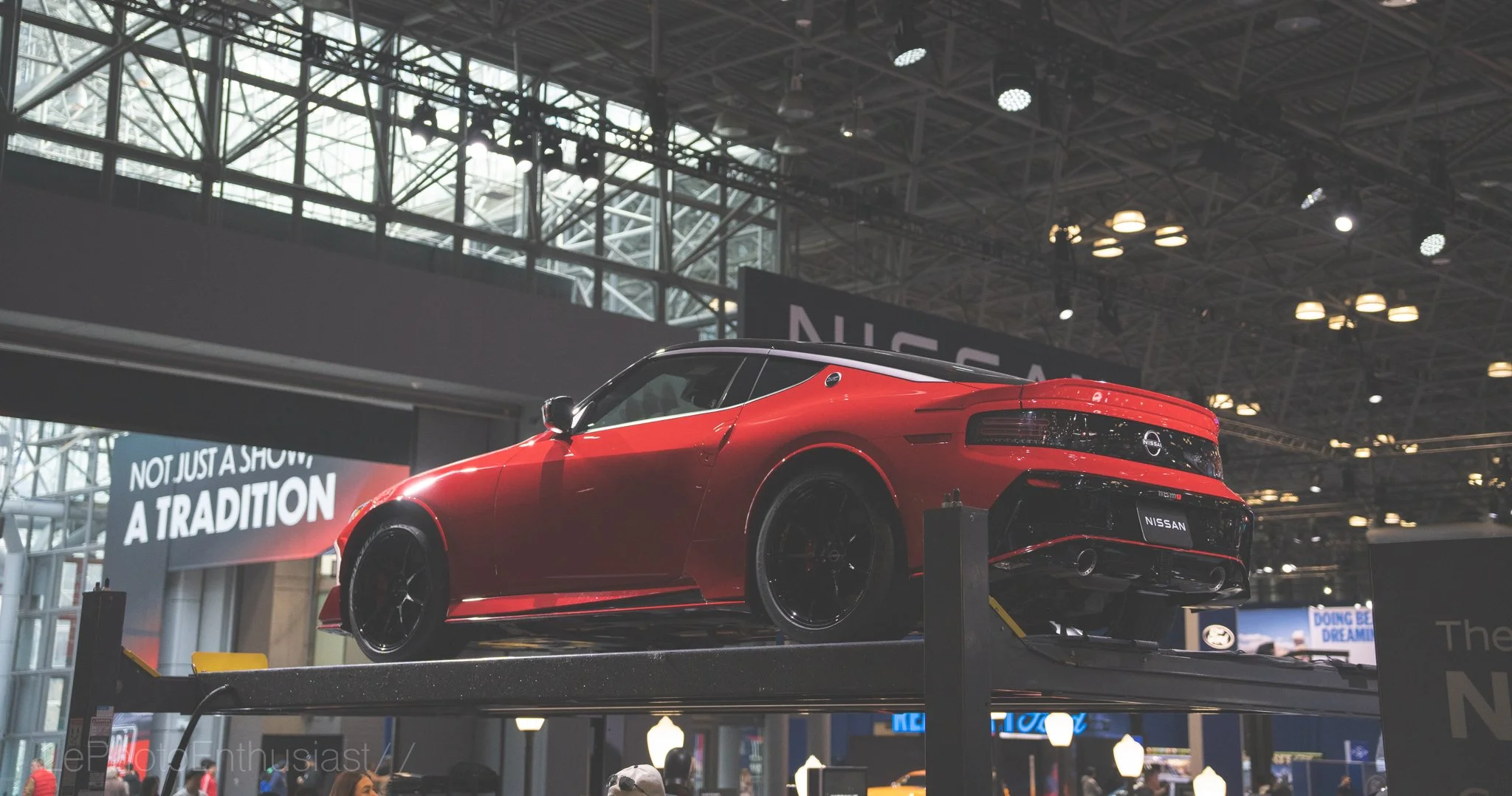 Red sports car displayed at an indoor auto show with signs and banners in the background.