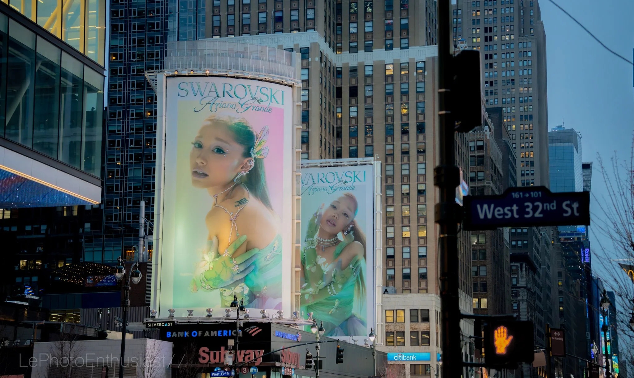 Billboard advertising Swarovski jewelry featuring a young girl with long hair, decorated with jewelry and accessories, set against a cityscape with tall buildings and a street sign for West 32nd Street.