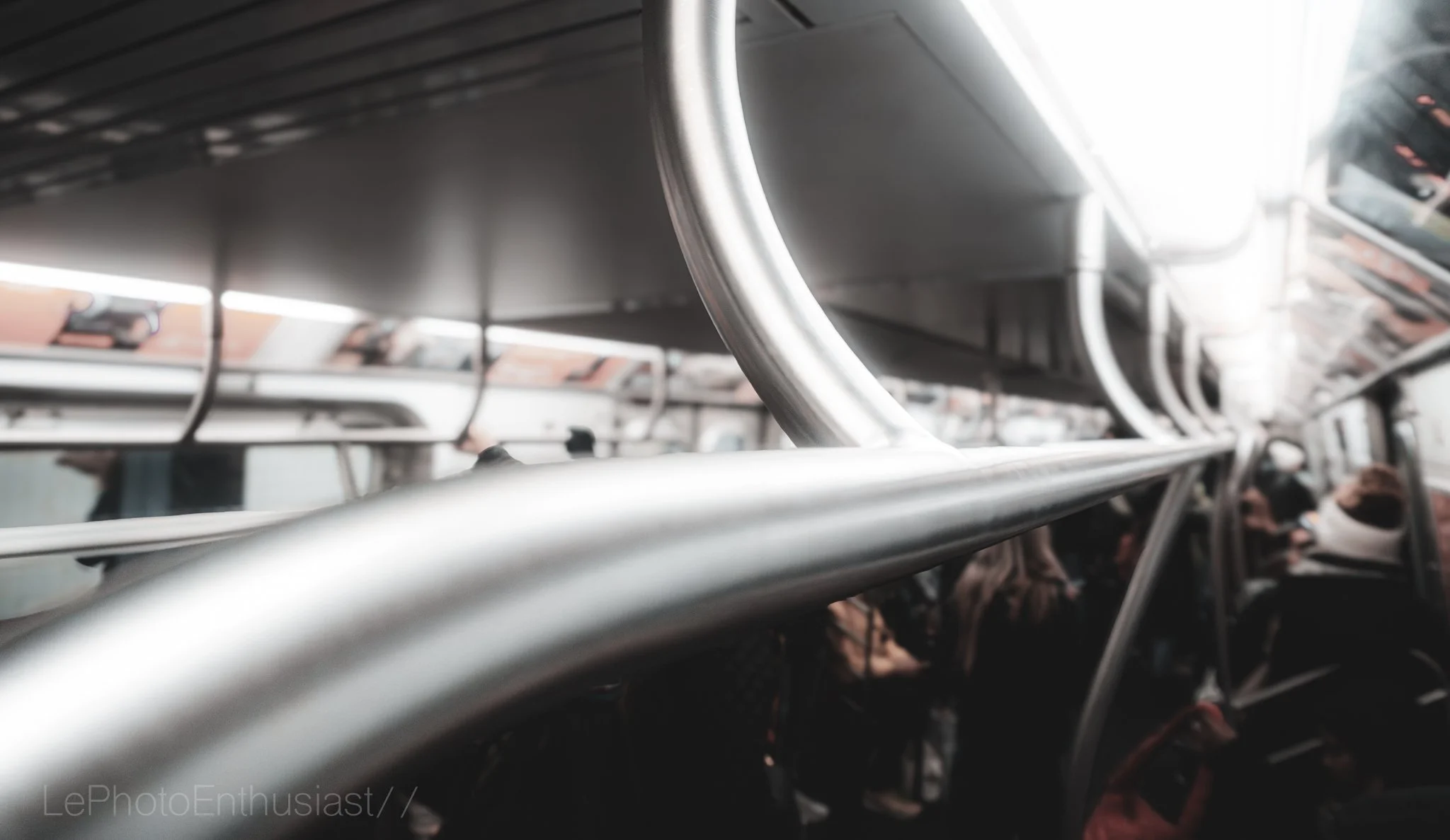 Interior view of a bus with metal handrails, and seats with passengers visible in the background.