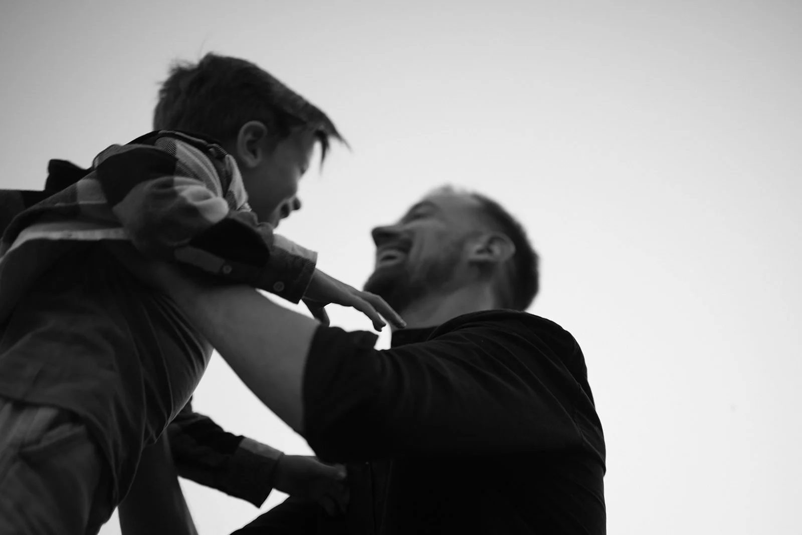 Zwei Männer lachen und spielen zusammen im Freien, eine Person hebt ein Kind hoch.