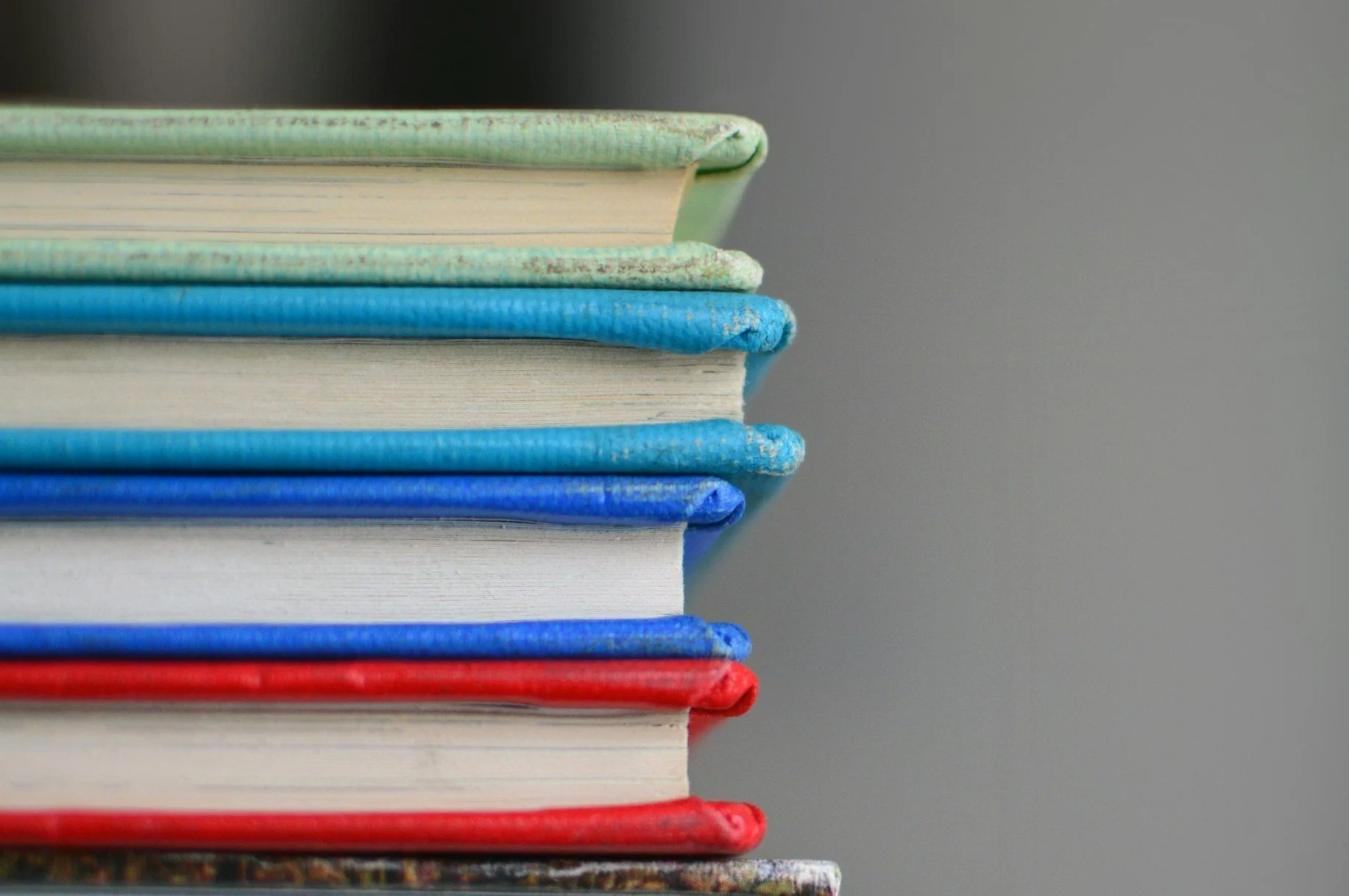 Stacked colorful hardcover books with different colored covers and worn edges.