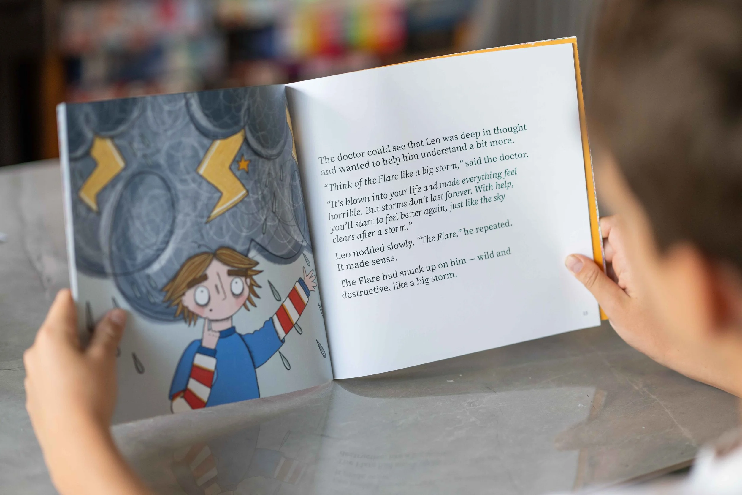 A person holding an open children's book The Flare: A Story About PANS PANDAS and Ways To Cope with illustrations of a young girl and storm clouds, along with text about helping Leo understand a storm.