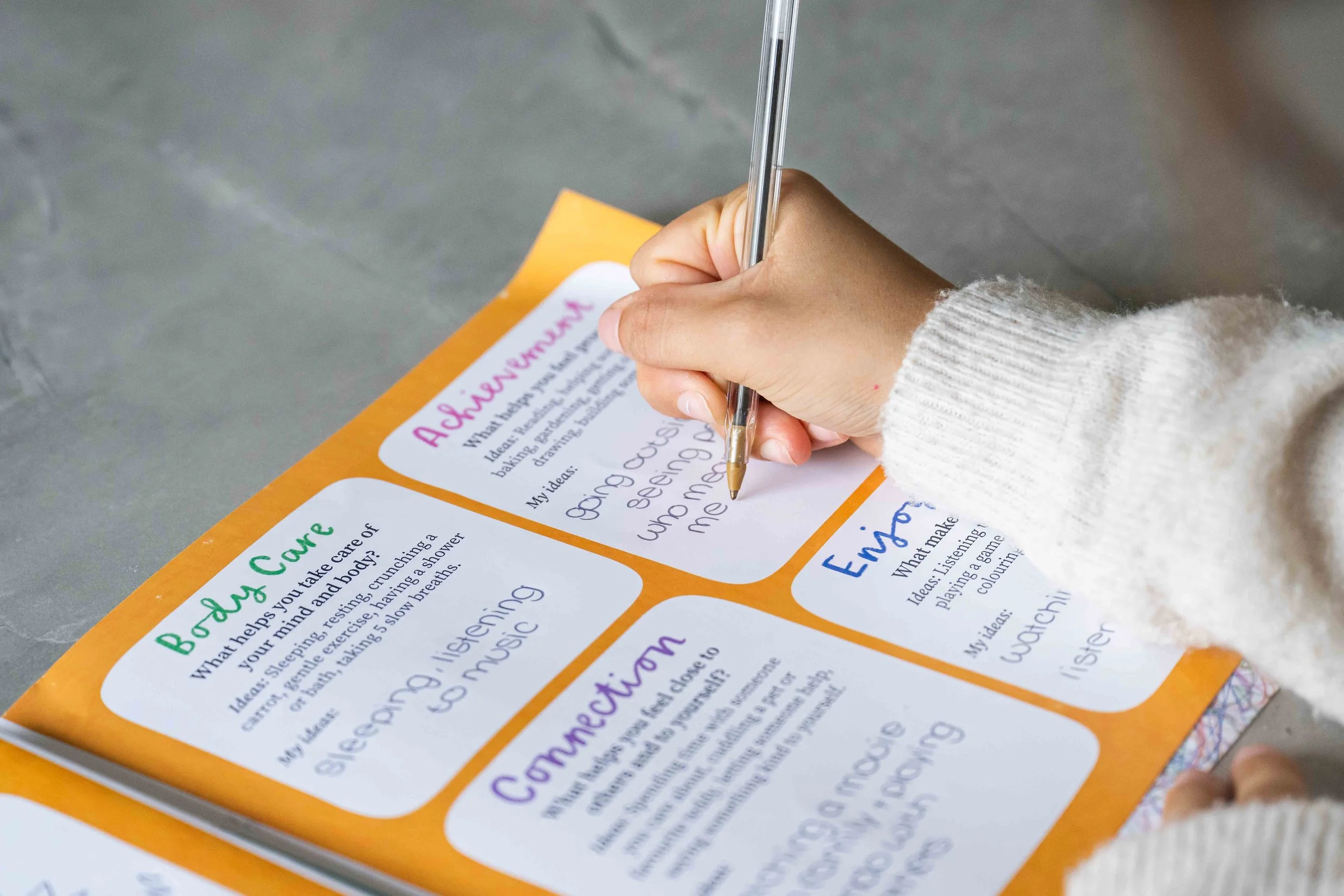 Close-up of a person's hand holding a clear pen and completing a personalised The Flare Survival Guide in the book The Flare: A Story About PANS PANDAS and Ways To Cope written by Dr Vicky Queralt, Clinical Psychologist