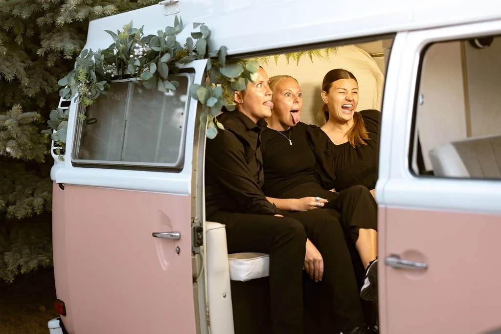 3 women dressed in black smiling and making silly faces in a photo booth bus