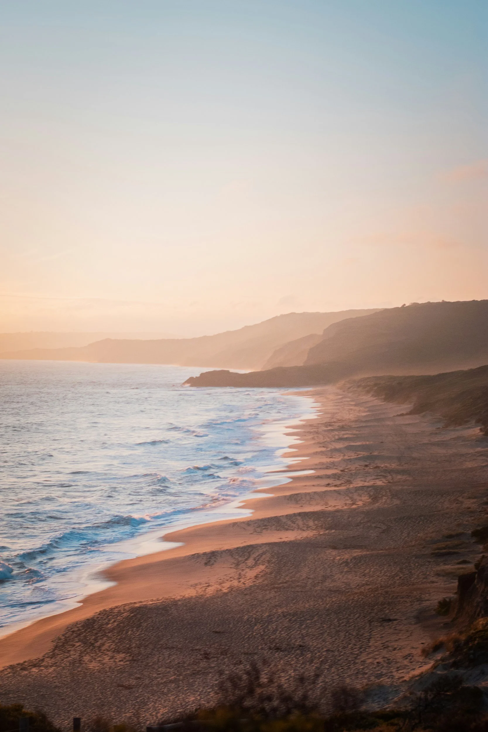 Scenic view of a sandy beach at sunset with gentle waves, cliffs, and hills in the distance providing the feeling of hope.