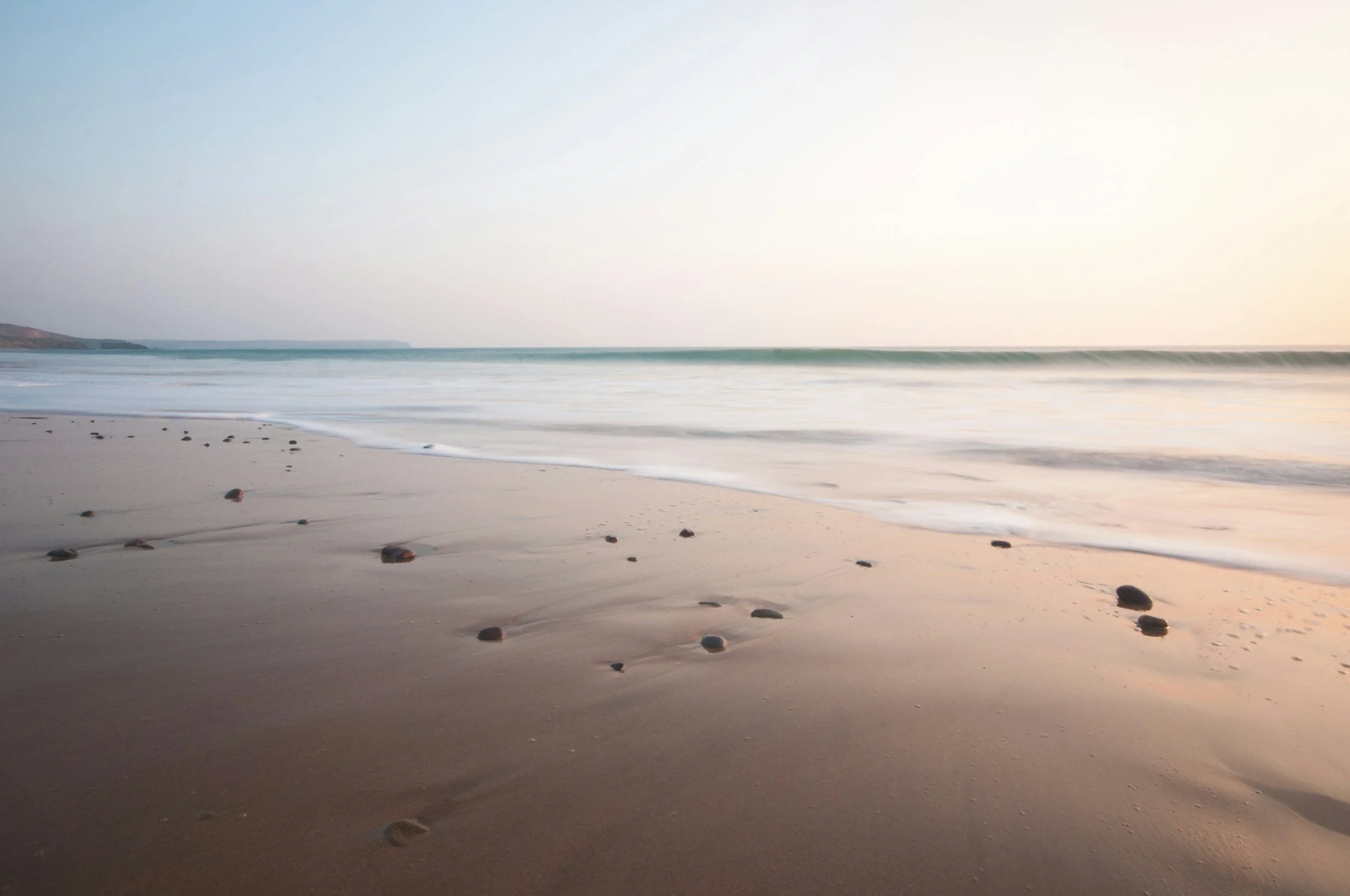 A peaceful beach at sunrise with gentle waves and scattered rocks on the sand symbolizing calmness.