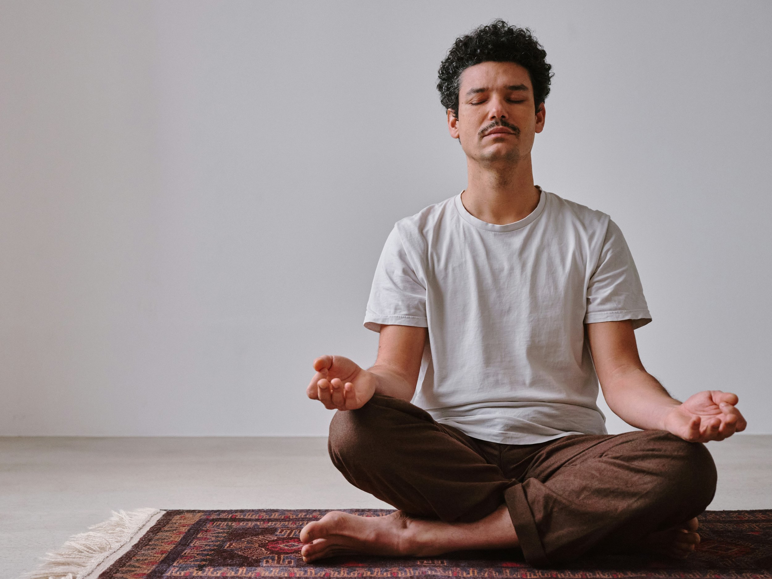 A man sitting cross-legged on a rug practicing meditation with eyes closed and hands resting on knees in a peaceful pose.