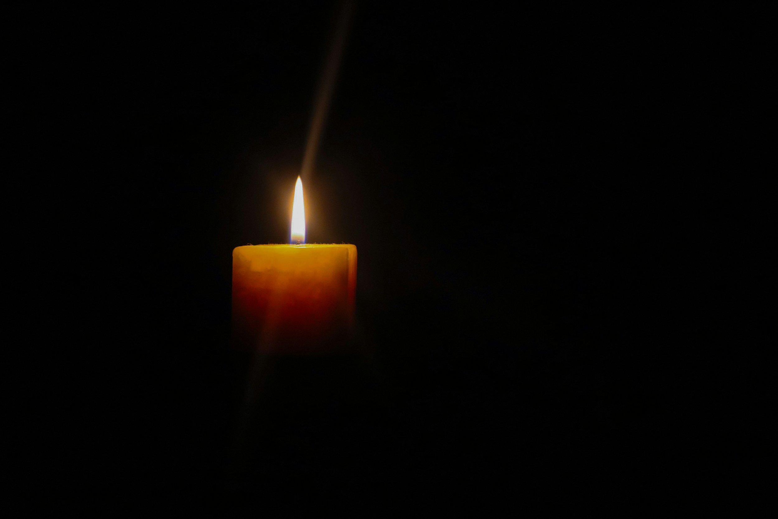 A single lit yellow candle against a dark background.