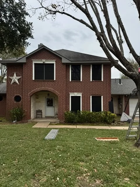Two-story brick house with a front porch, large windows, and a tree in the front yard, with a ladder leaning against the house.